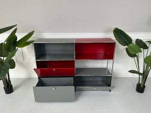 Gebrauchtes USM Haller Designer Regal in den Farben Rot und Grau vor einer Wand, stilvoll und modern eingerichtet.