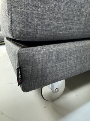 Gebrauchtes graues Brühl Fourtwo Designer Stoff Ecksofa vor einer Wand, stilvoll und modern eingerichtet.