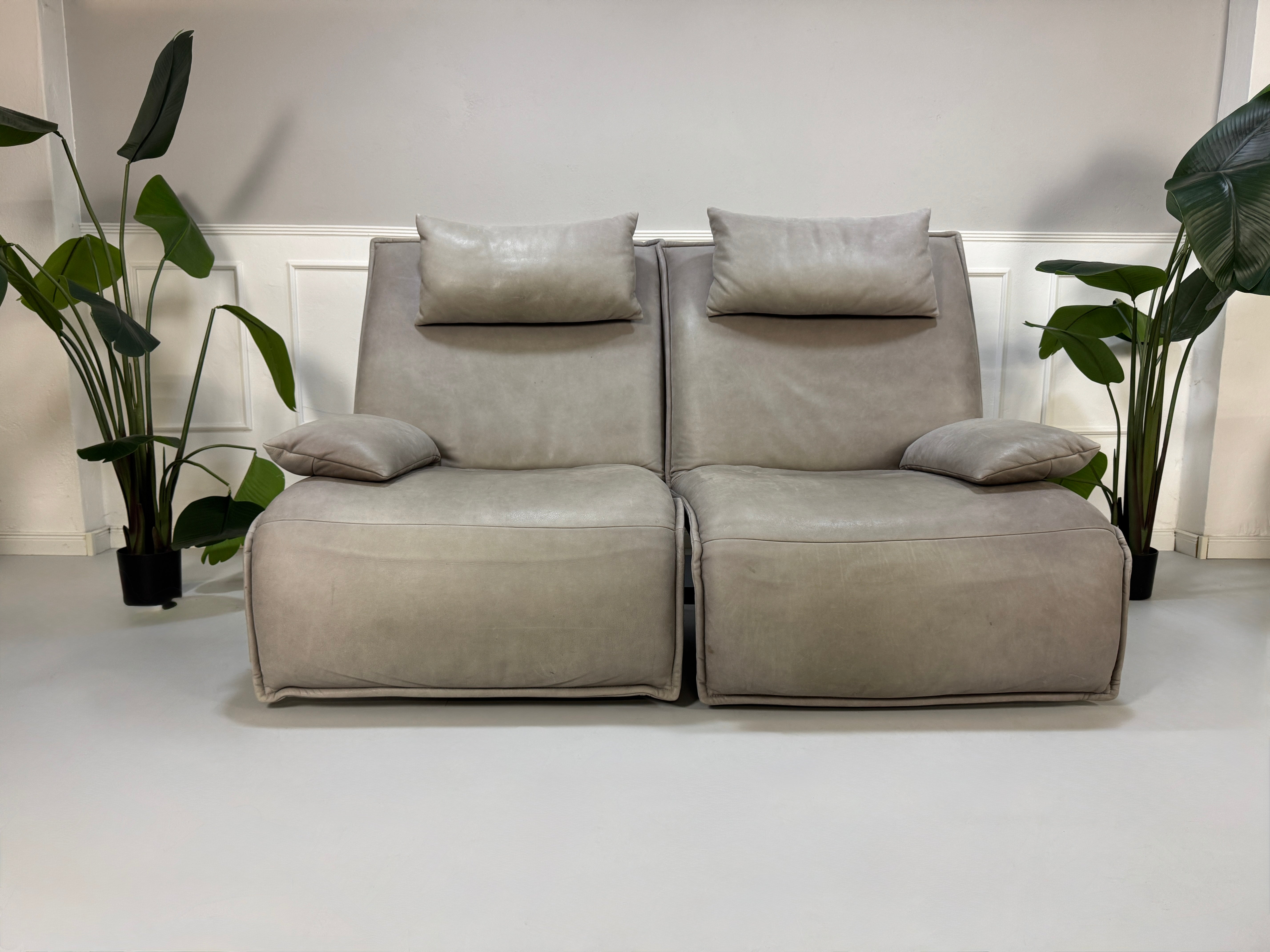 Gebrauchtes graues Ledersofa Koinor Modell Evia vor einer modernen Wand.