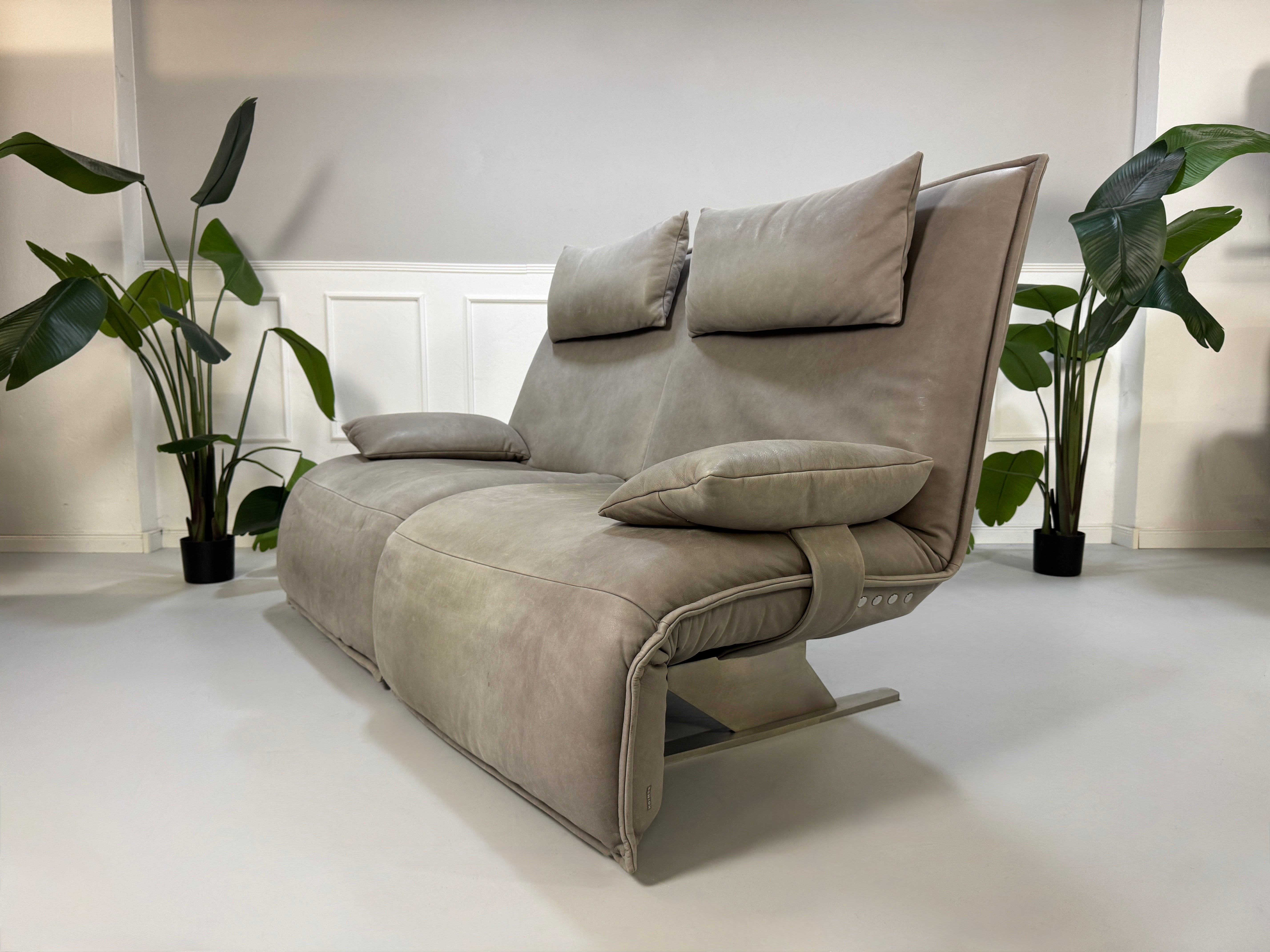 Gebrauchtes graues Ledersofa Koinor Modell Evia vor einer modernen Wand.