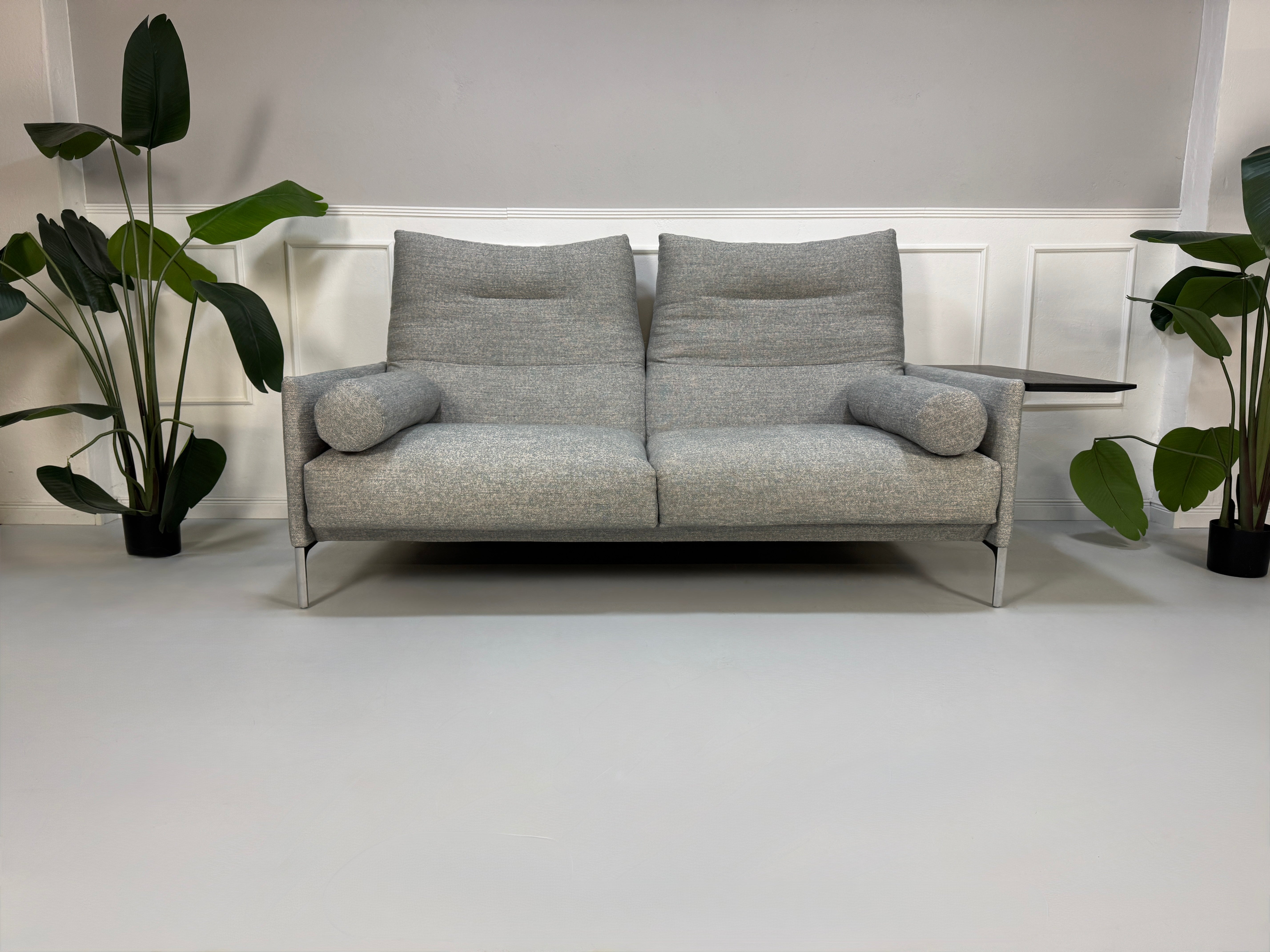 Gebrauchtes graues Stoffsofa mit einem Hocker von COR Modell Avalanche vor einer modernen Wand.
