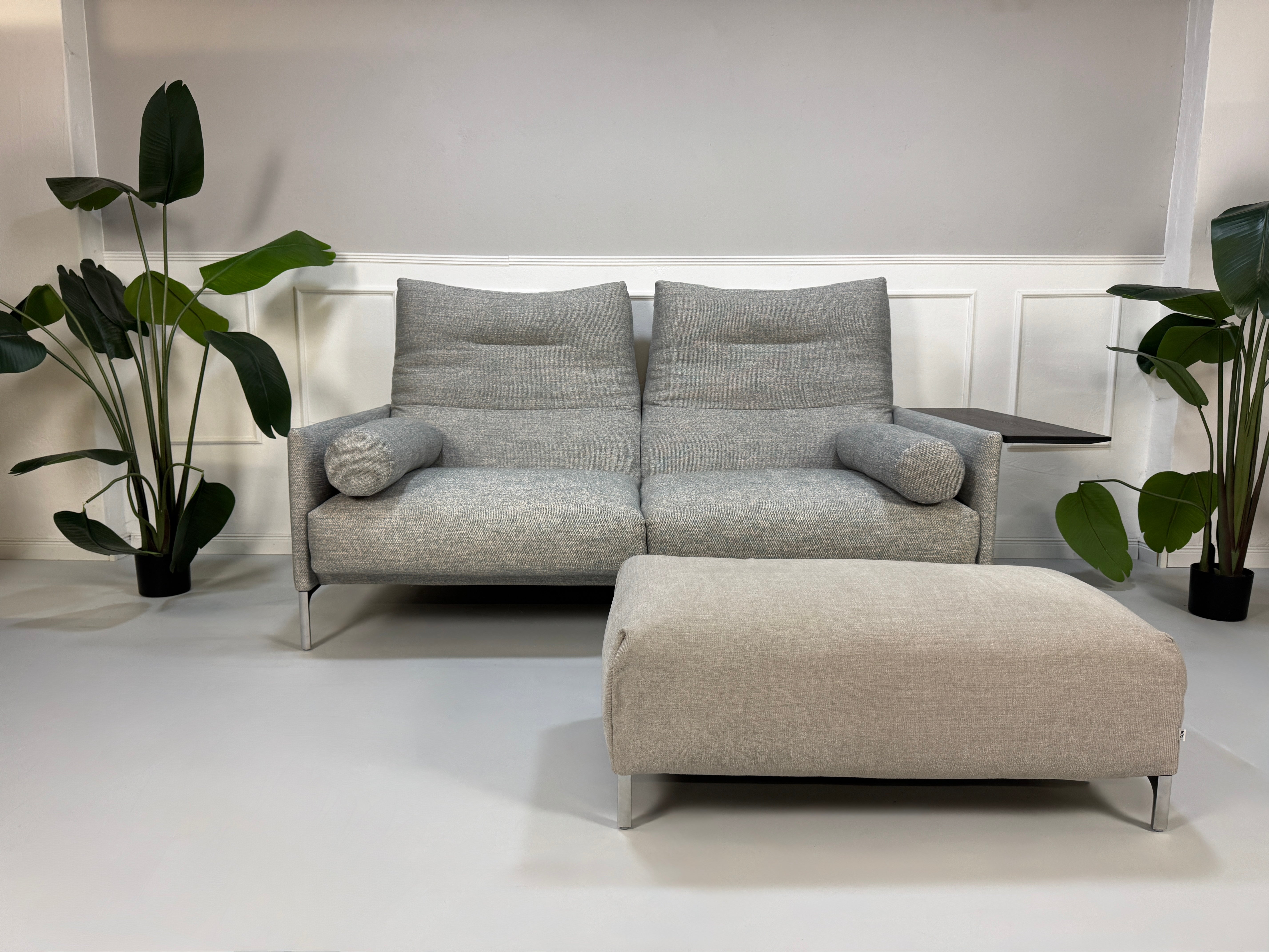 Gebrauchtes graues Stoffsofa mit einem Hocker von COR Modell Avalanche vor einer modernen Wand.