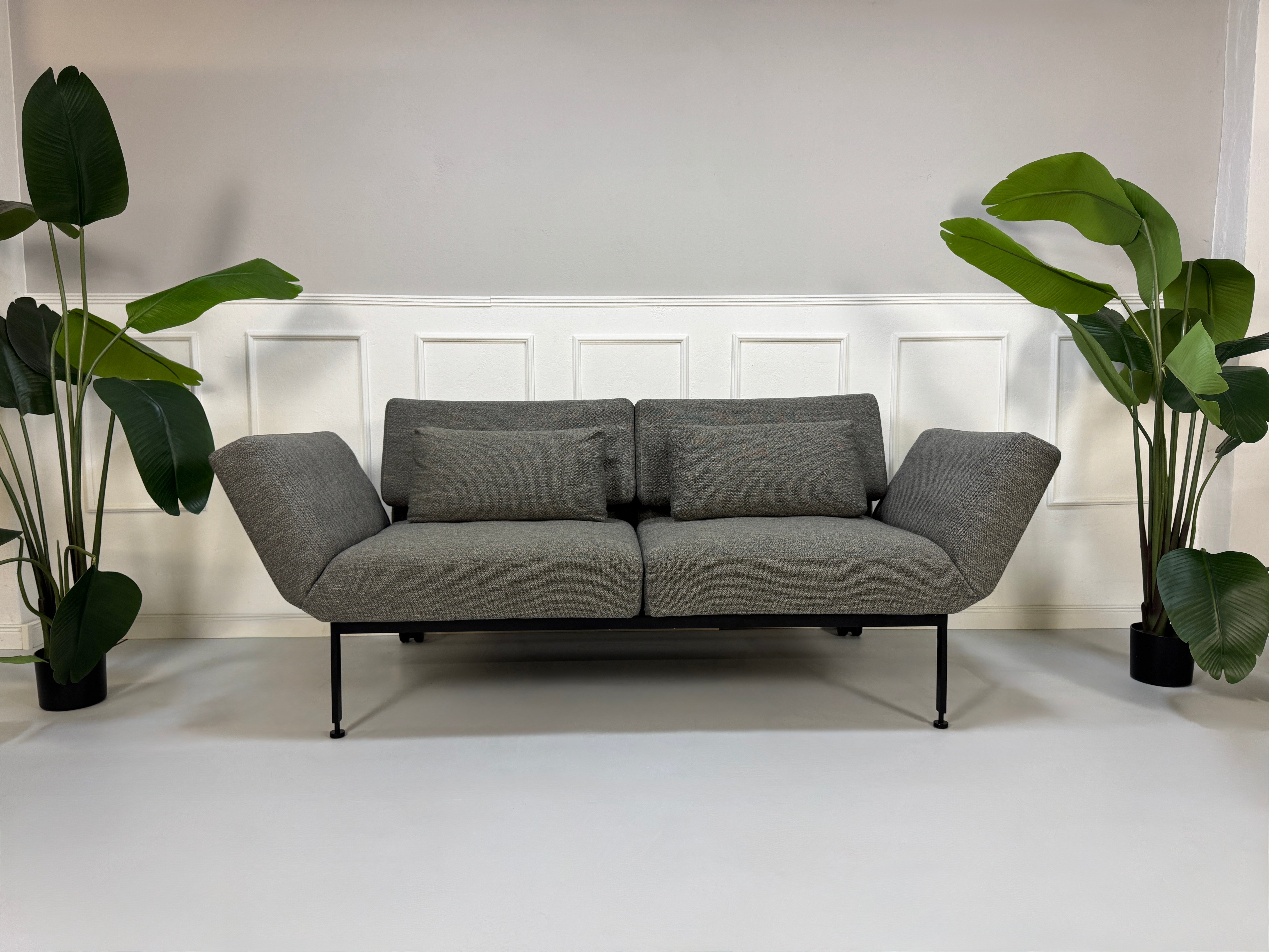 Gebrauchtes graues Stoffsofa Brühl Modell Roro Soft vor einer modernen Wand.