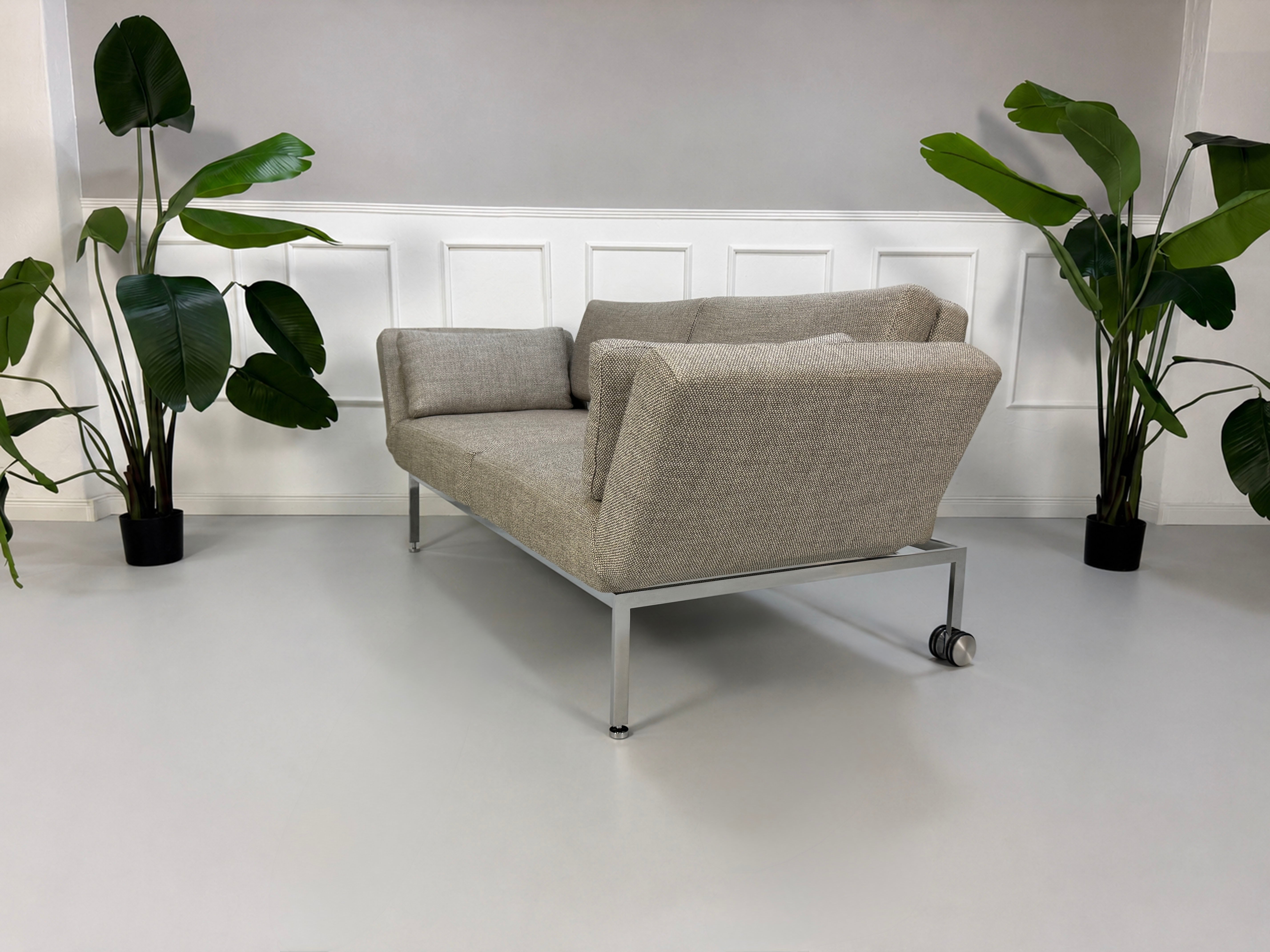 Gebrauchtes graues Brühl Roro Soft Designer Stoff Sofa vor einer Wand, stilvoll und modern eingerichtet.