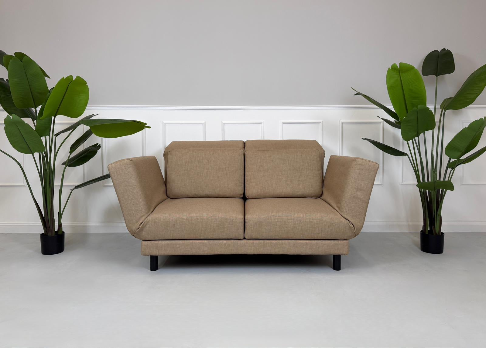 Gebrauchtes braunes Stoffsofa Brühl Modell Moule Small vor einer modernen Wand.