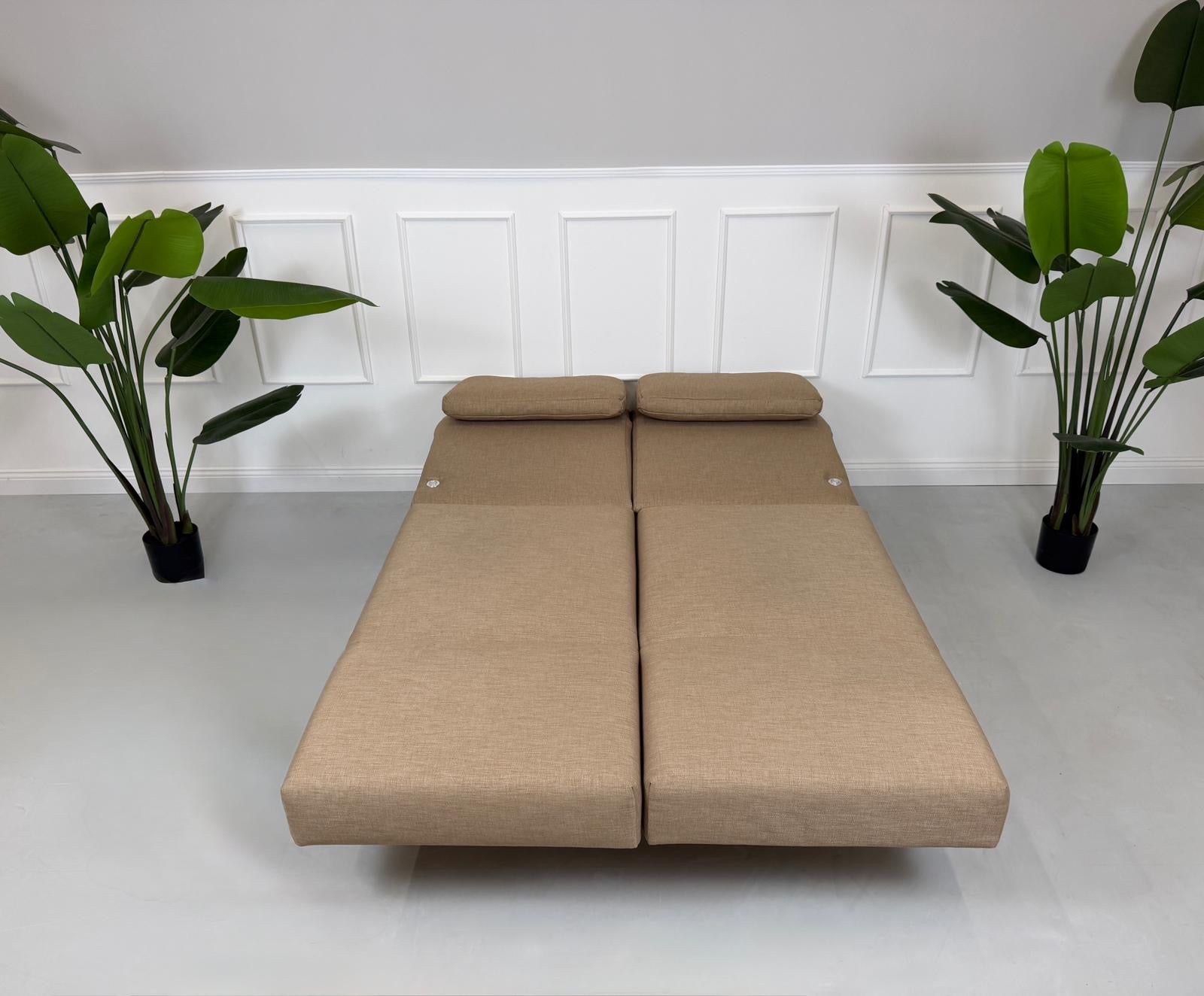 Gebrauchtes braunes Stoffsofa Brühl Modell Moule Small vor einer modernen Wand.
