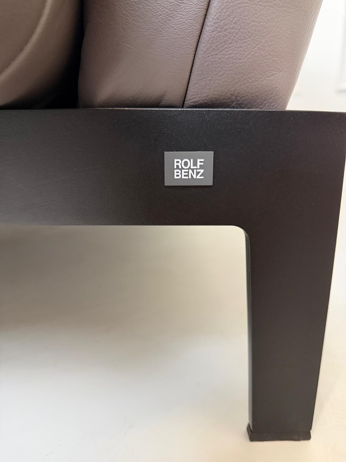 Gebrauchtes braunes Ledersofa Rolf Benz Modell Mera vor einer modernen Wand.