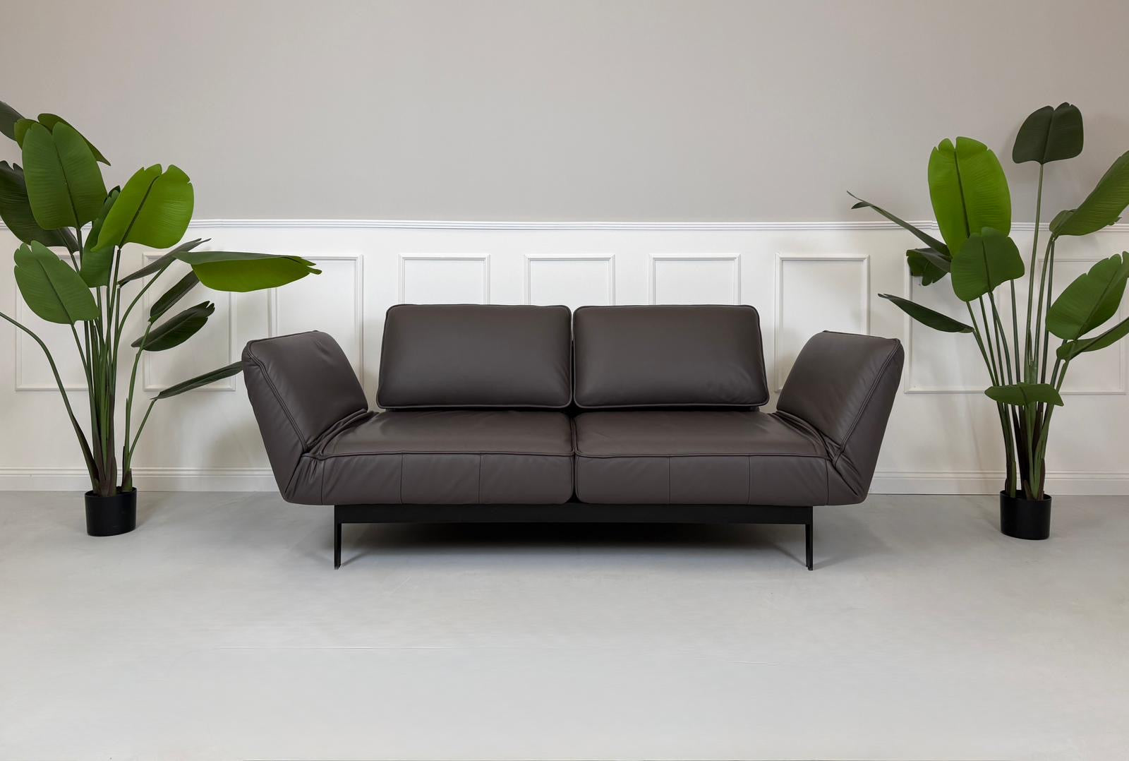 Gebrauchtes braunes Ledersofa Rolf Benz Modell Mera vor einer modernen Wand.