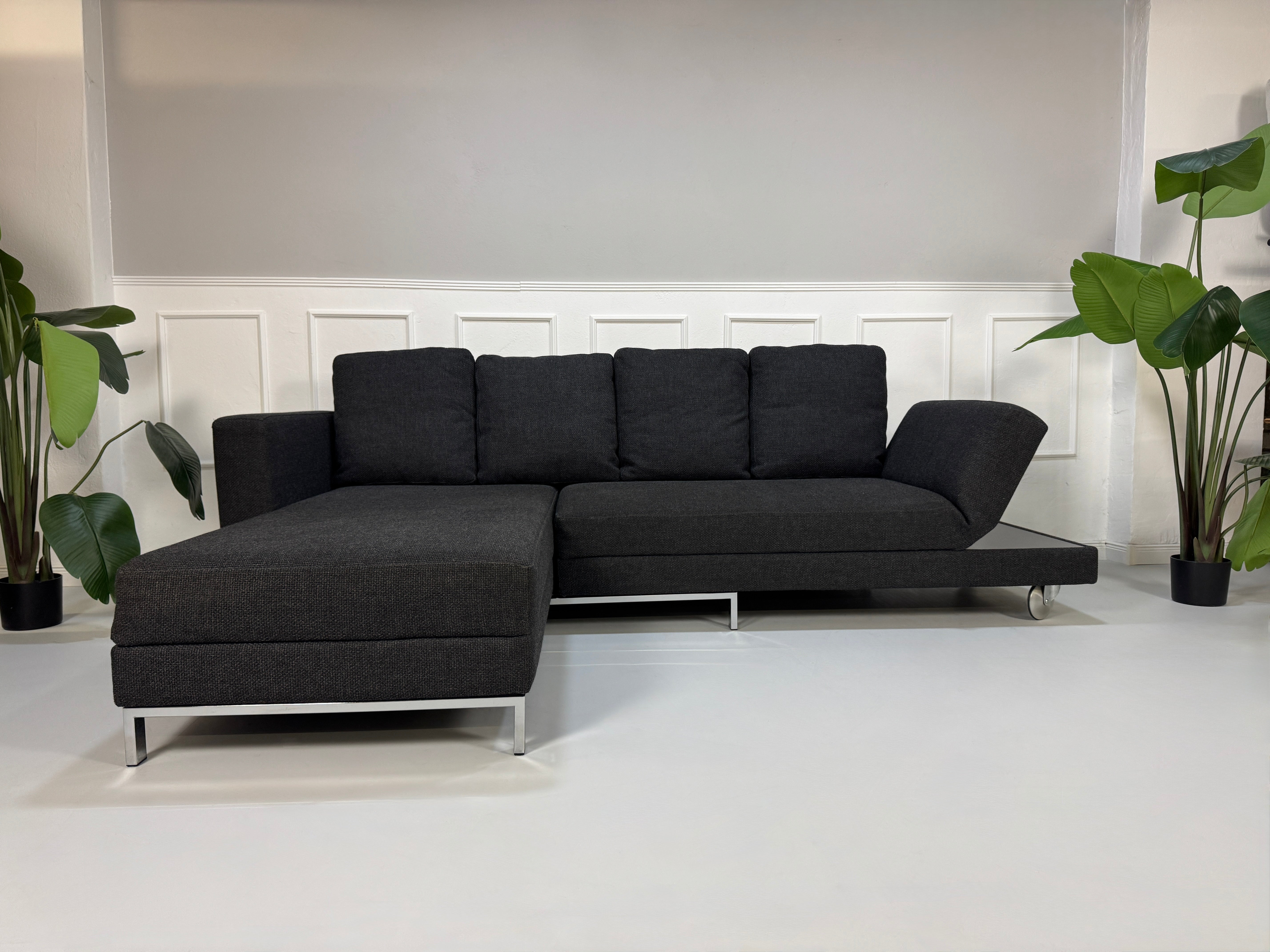 Gebrauchtes graues Stoffsofa Brühl Modell FourTwo vor einer modernen Wand.