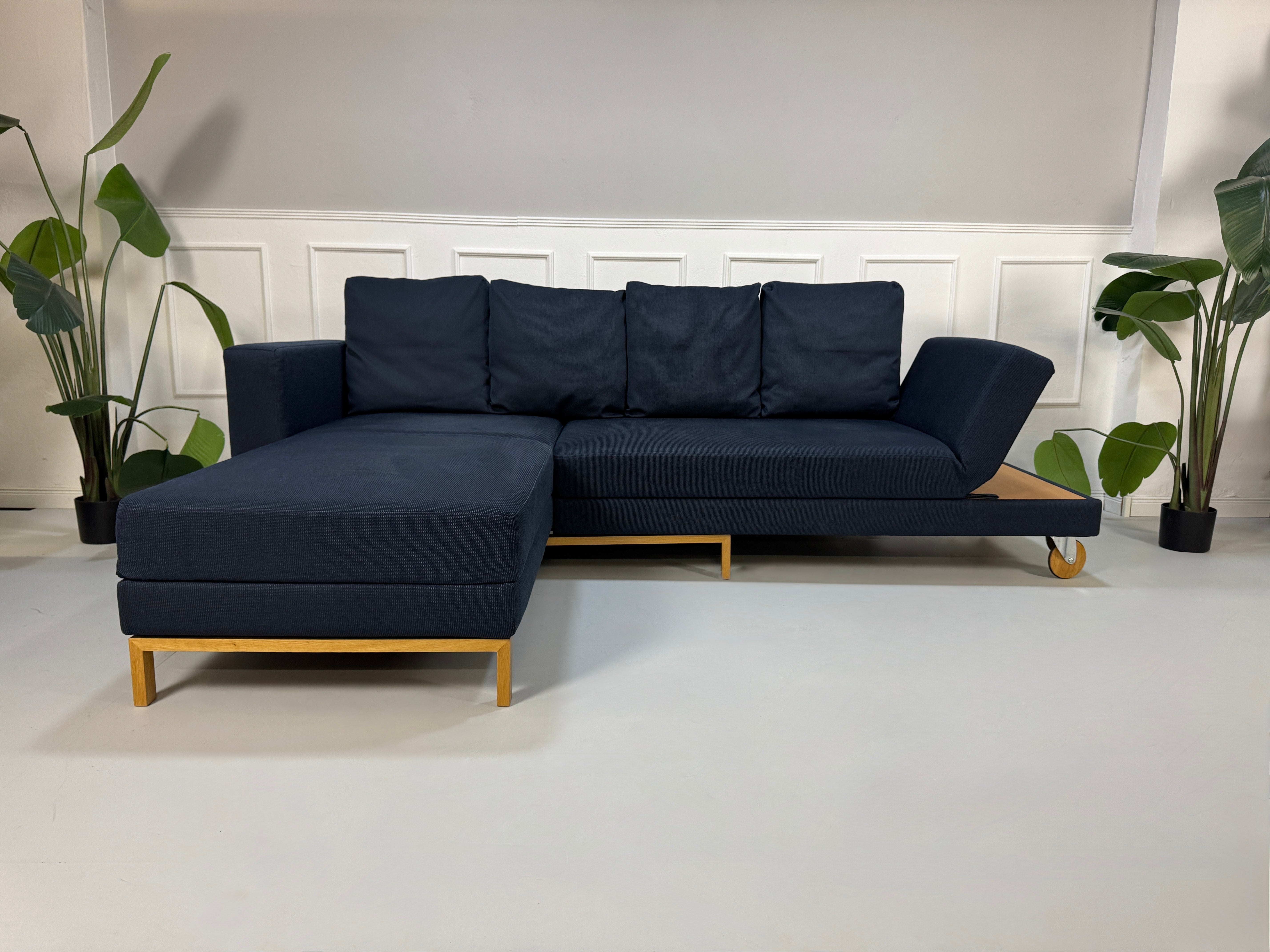 Gebrauchtes blaues Stoffsofa Brühl Modell Fourtwo vor einer modernen Wand.