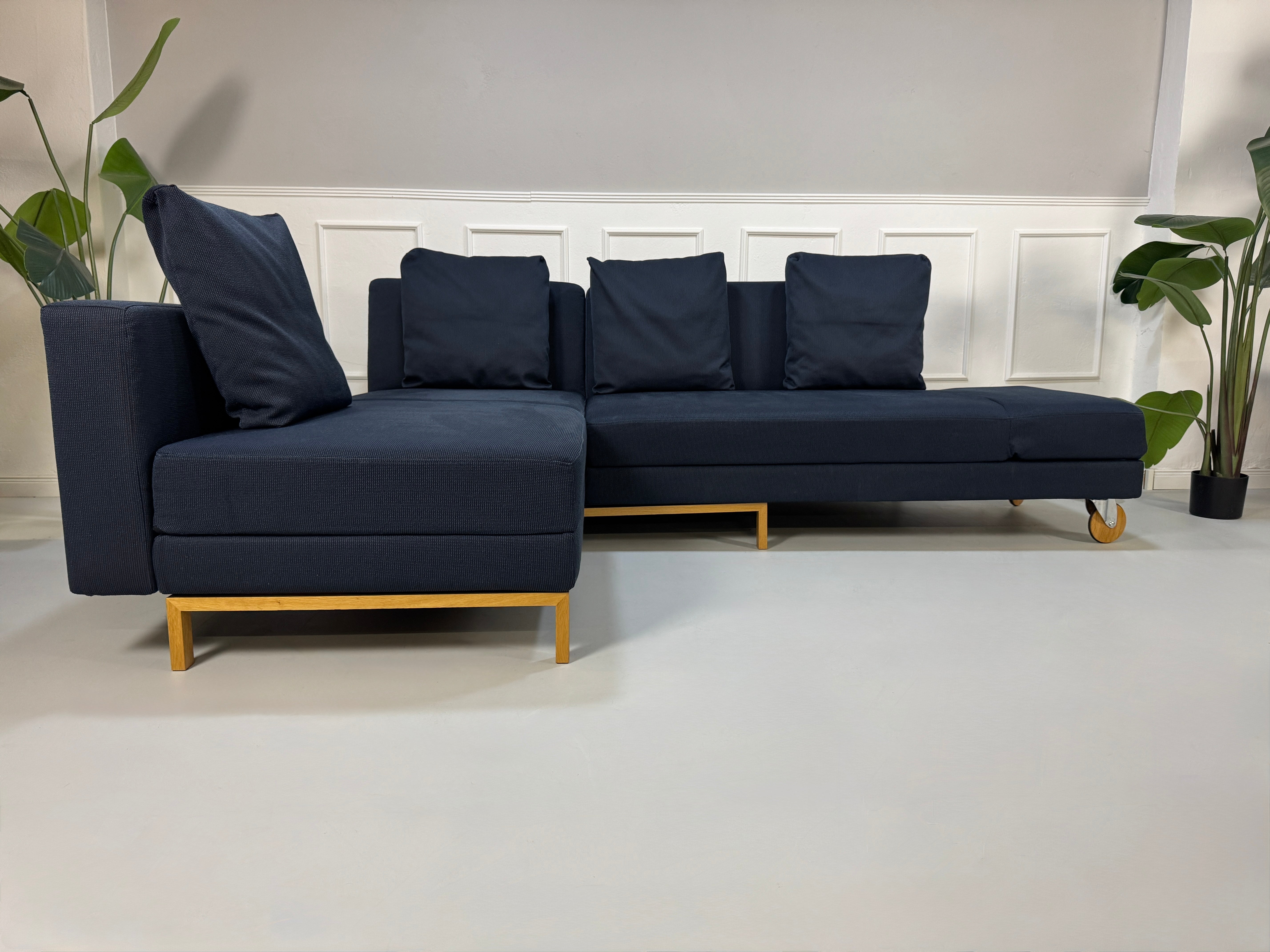 Gebrauchtes blaues Stoffsofa Brühl Modell Fourtwo vor einer modernen Wand.