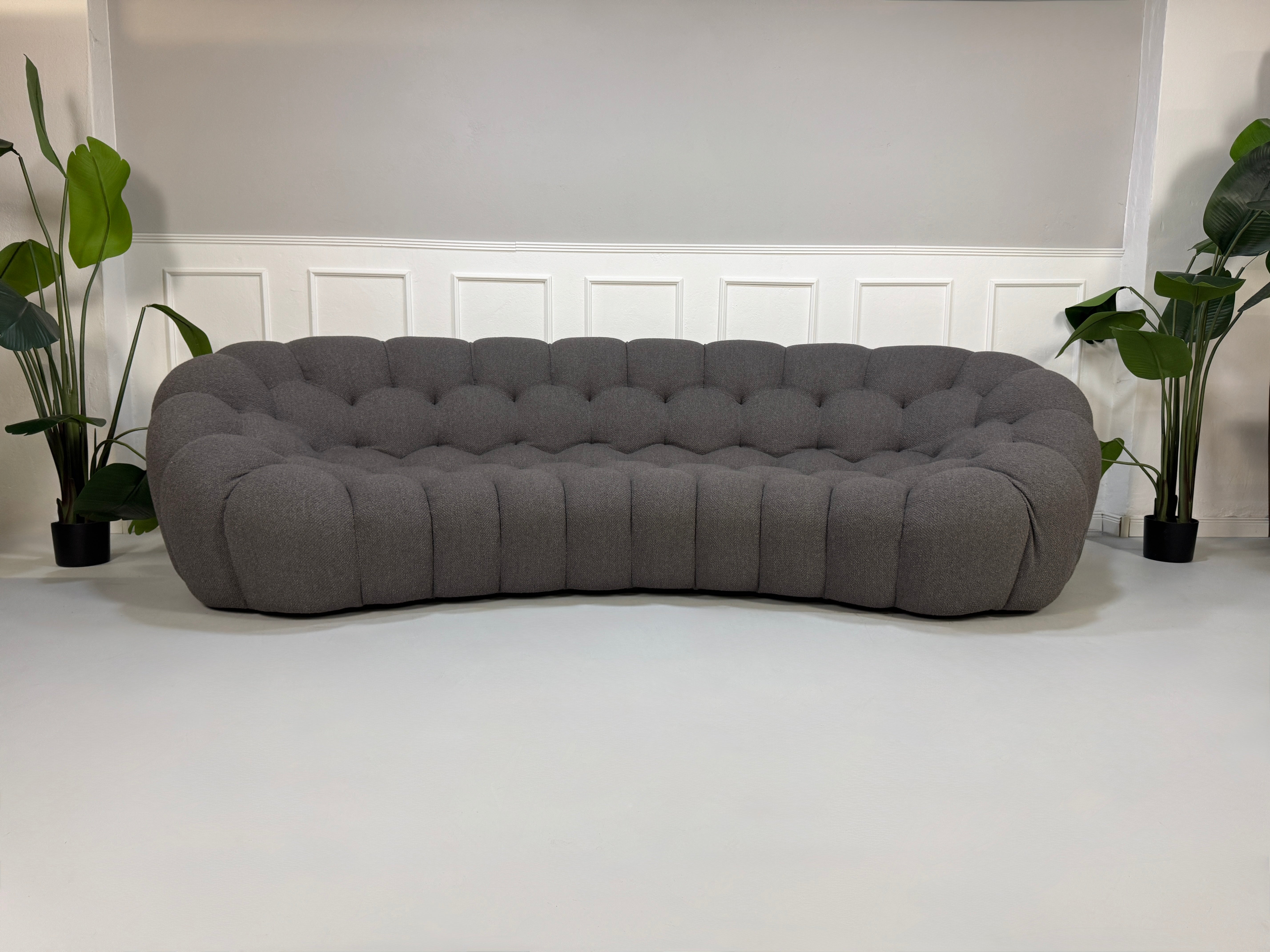 Gebrauchtes graues Stoffsofa Roche Bobois Modell Bubble vor einer modernen Wand.