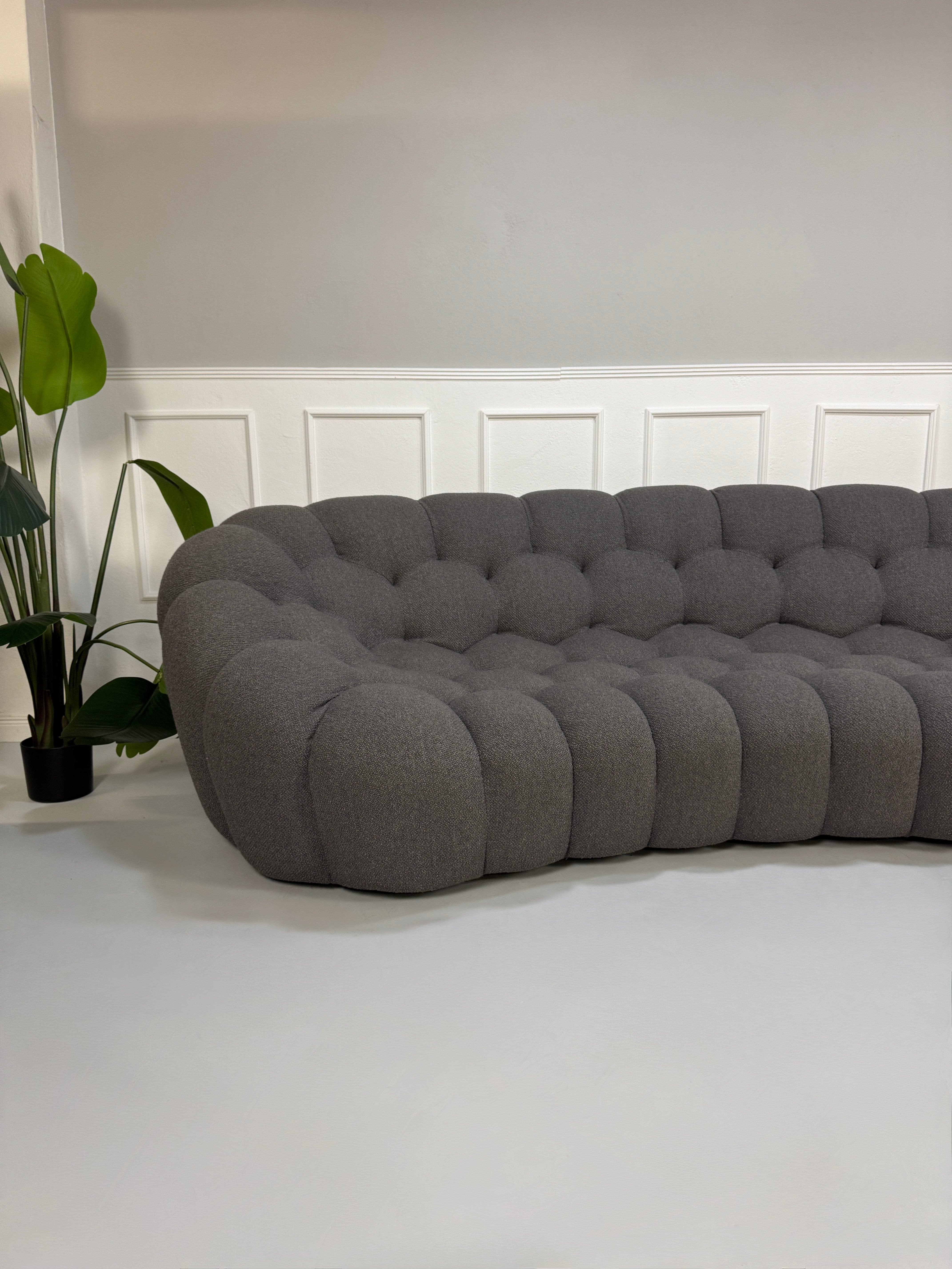 Gebrauchtes graues Stoffsofa Roche Bobois Modell Bubble vor einer modernen Wand.