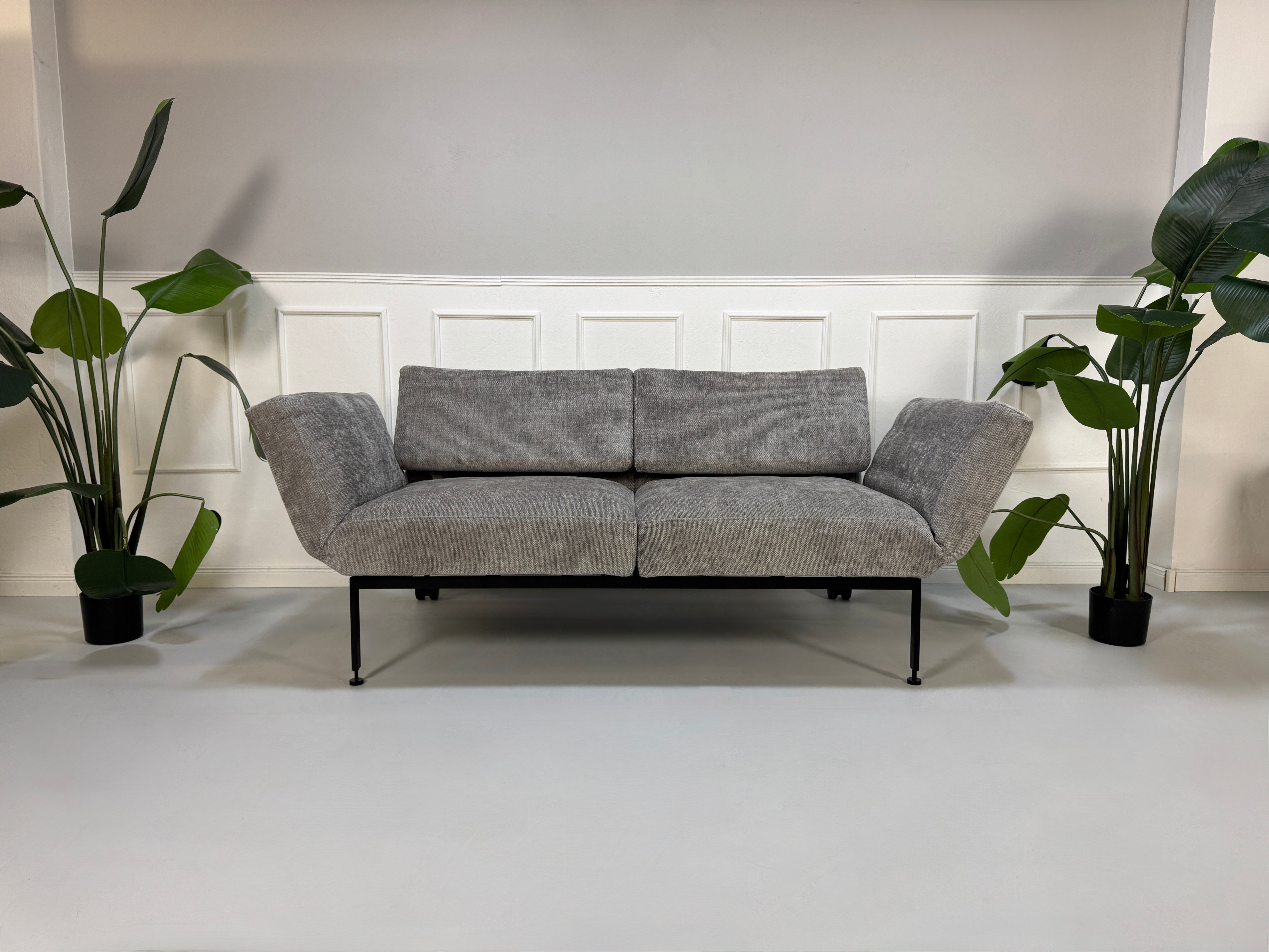 Gebrauchtes graues Stoffsofa Brühl Modell Roro Spring vor einer modernen Wand.