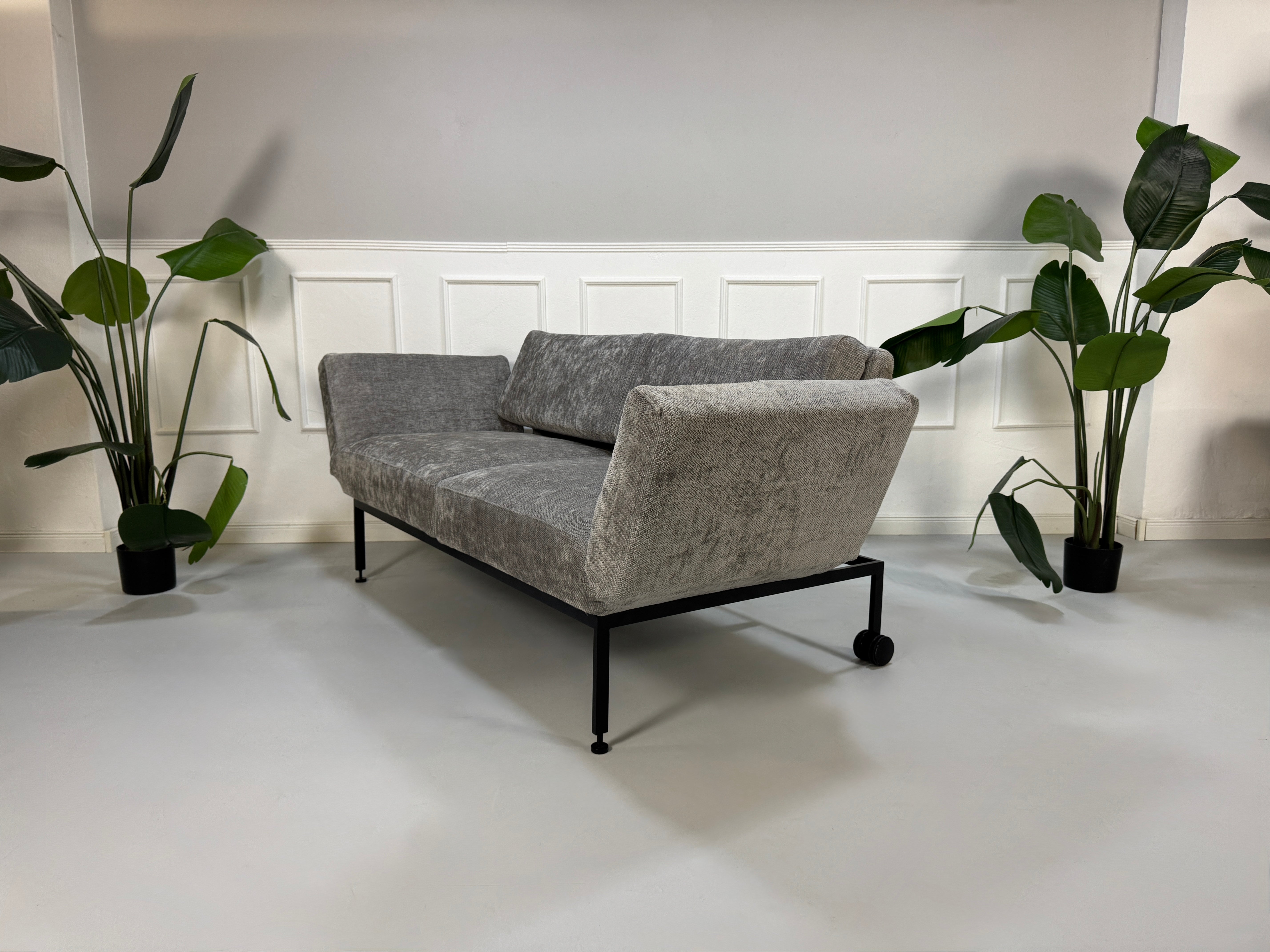 Gebrauchtes graues Stoffsofa Brühl Modell Roro Spring vor einer modernen Wand.