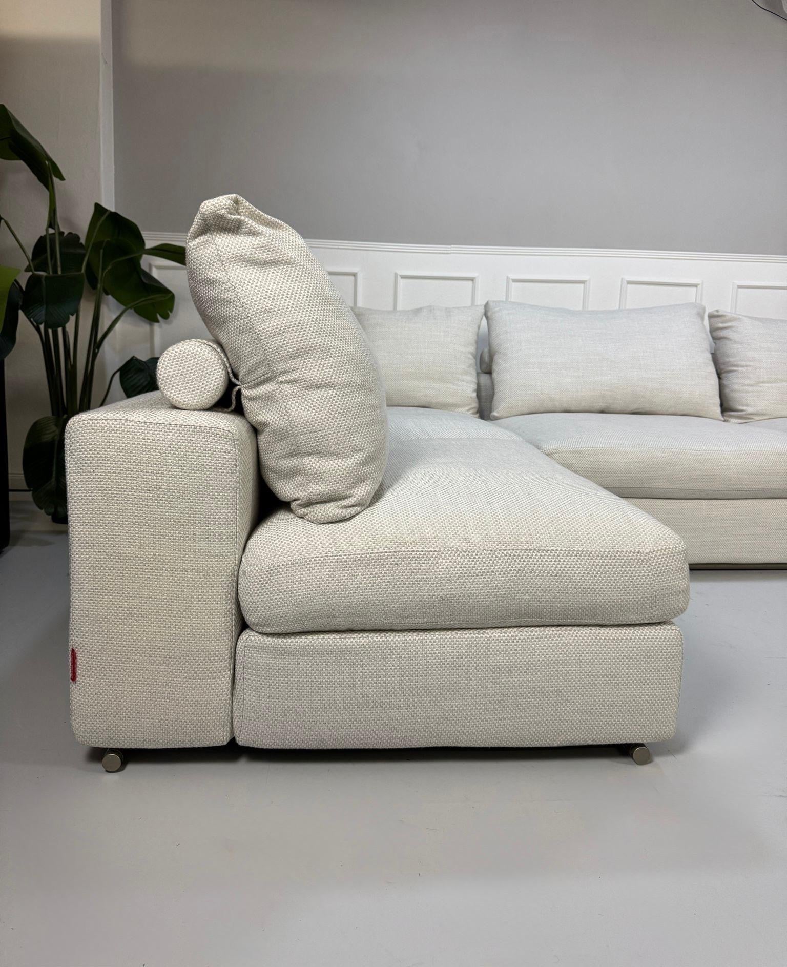 Gebrauchtes weißes Stoffsofa Flexform Modell Groundpiece vor einer modernen Wand.