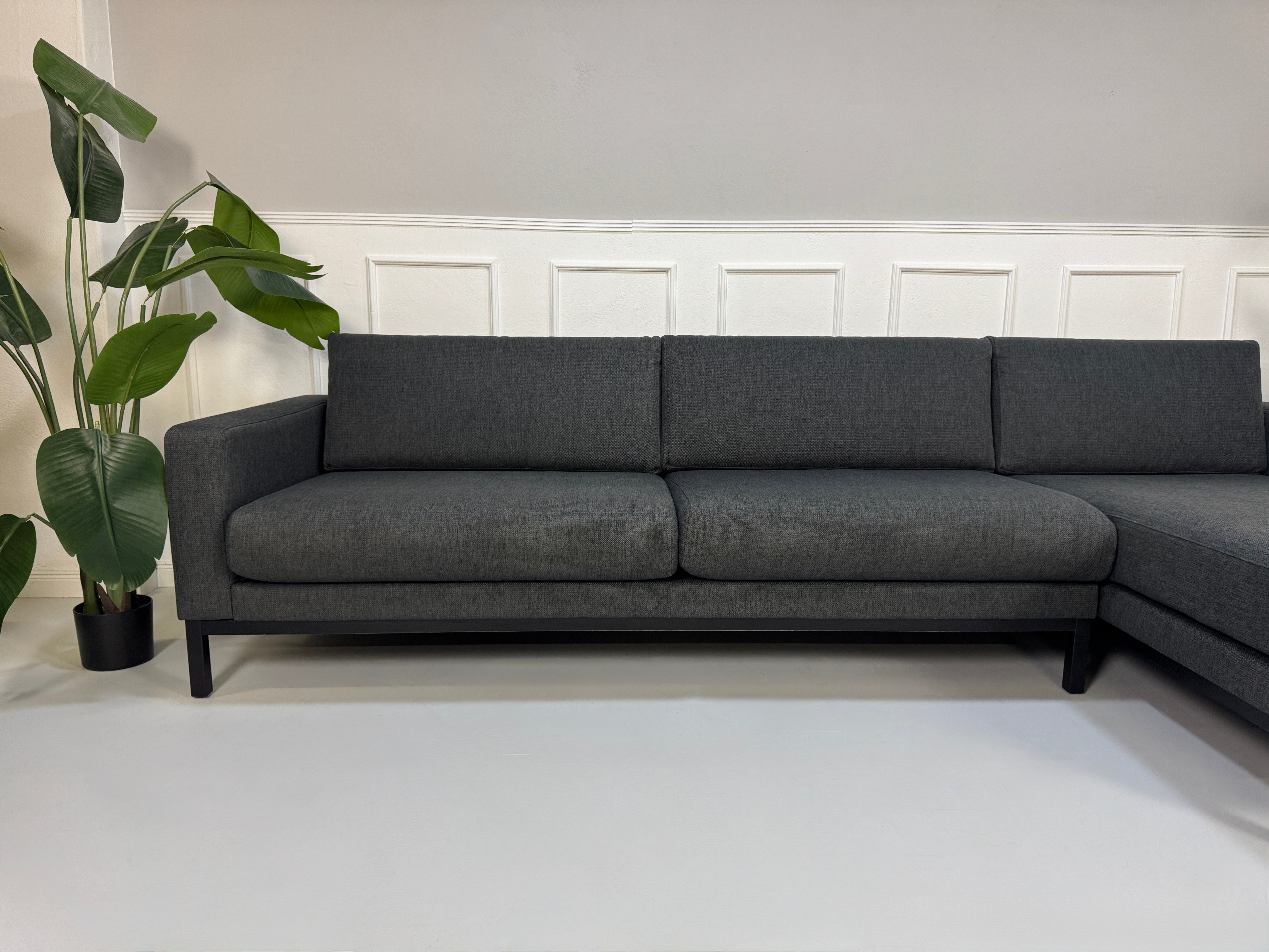 Gebrauchtes graues Stoffsofa Bolia Modell North vor einer modernen Wand.