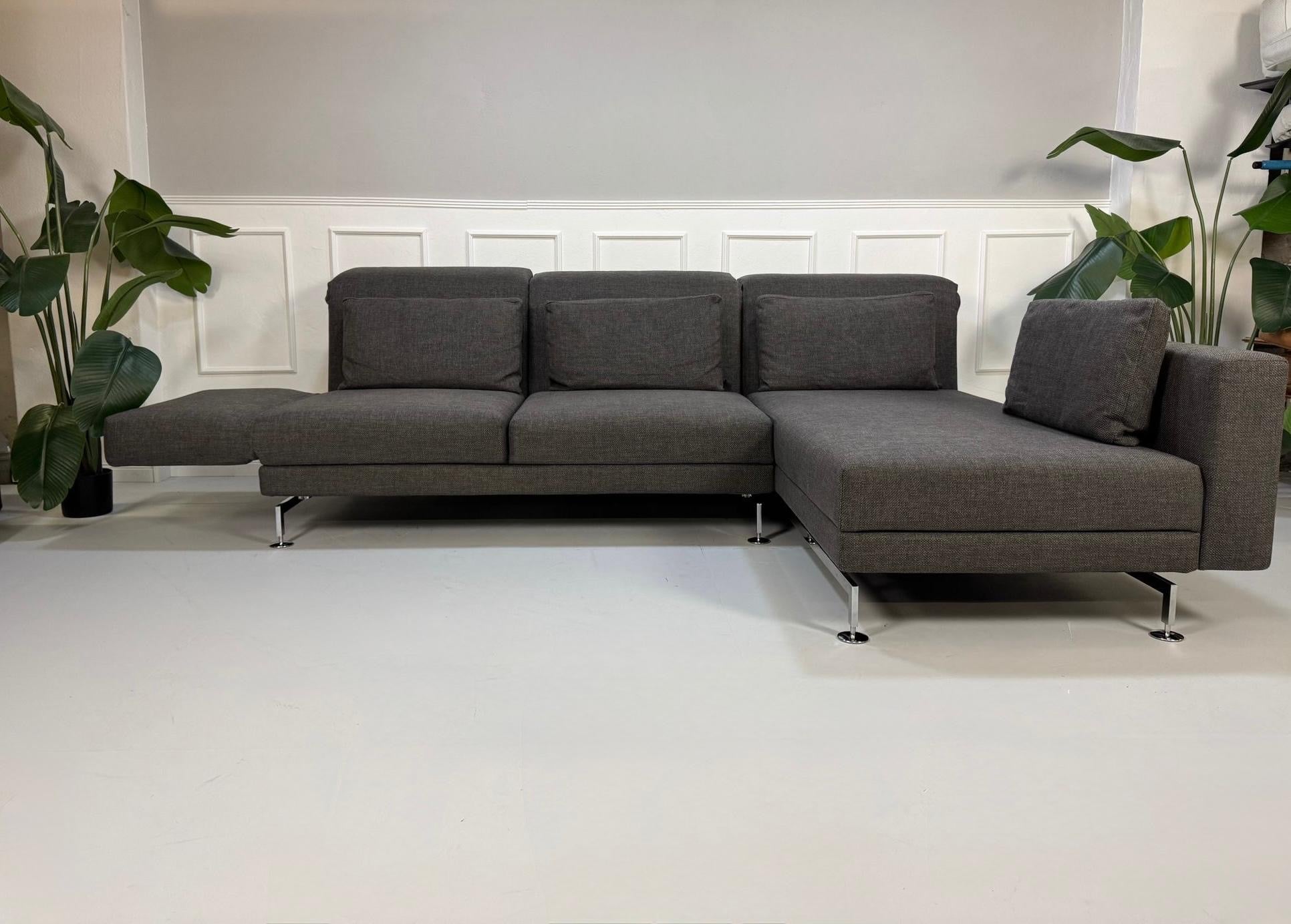 Gebrauchtes graues Stoffsofa Brühl Modell Moule vor einer modernen Wand.