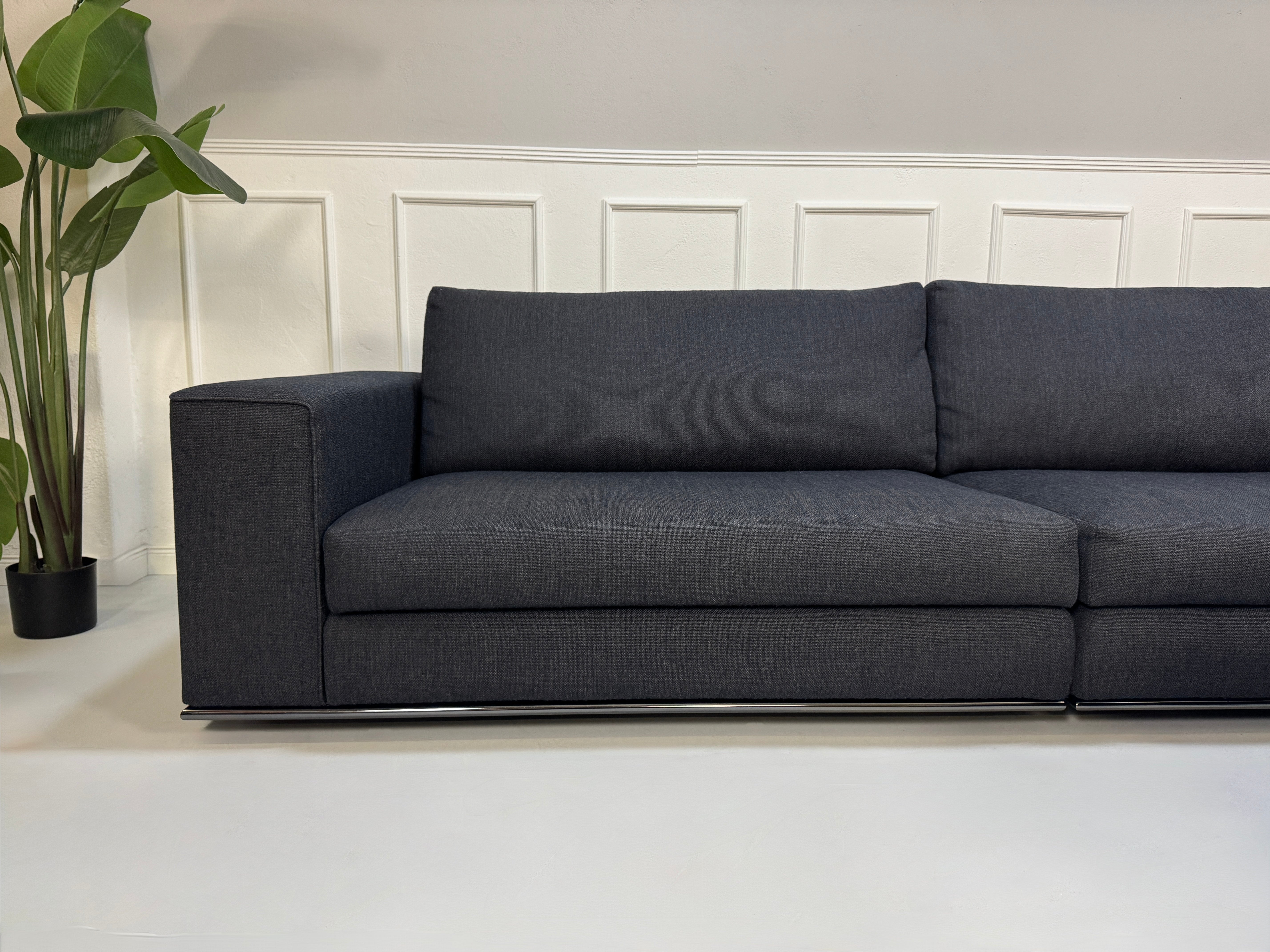 Gebrauchtes blau graues Minotti Hamilton Designer Stoff Sofa mit einem Hocker vor einer Wand, stilvoll und modern eingerichtet.