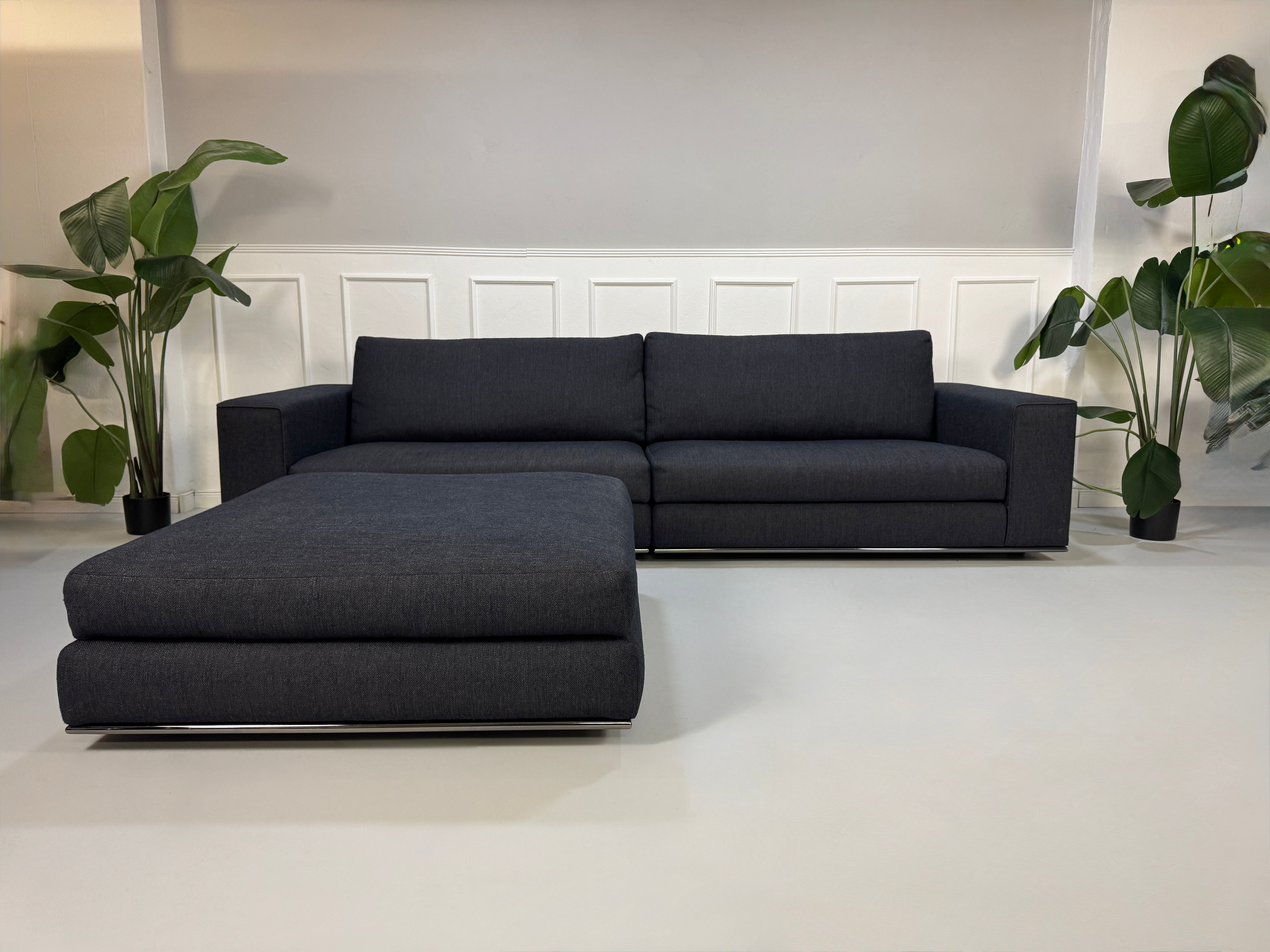 Gebrauchtes blau graues Minotti Hamilton Designer Stoff Sofa mit einem Hocker vor einer Wand, stilvoll und modern eingerichtet.