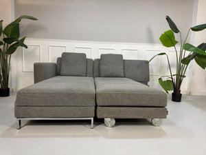 Gebrauchtes graues Brühl Fourtwo Designer Stoff Sofa vor einer Wand, stilvoll und modern eingerichtet.