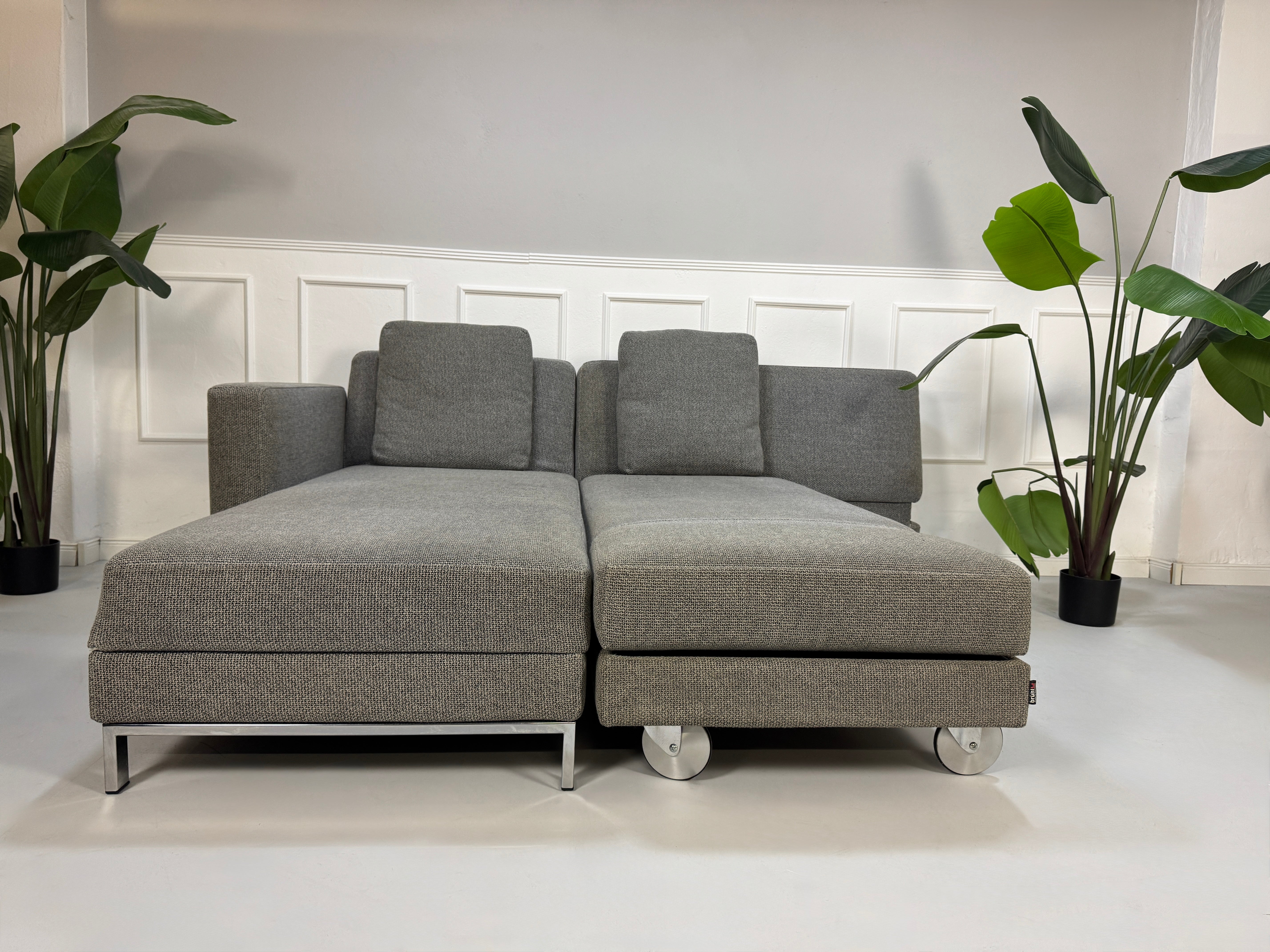 Gebrauchtes graues Brühl Fourtwo Designer Stoff Sofa vor einer Wand, stilvoll und modern eingerichtet.