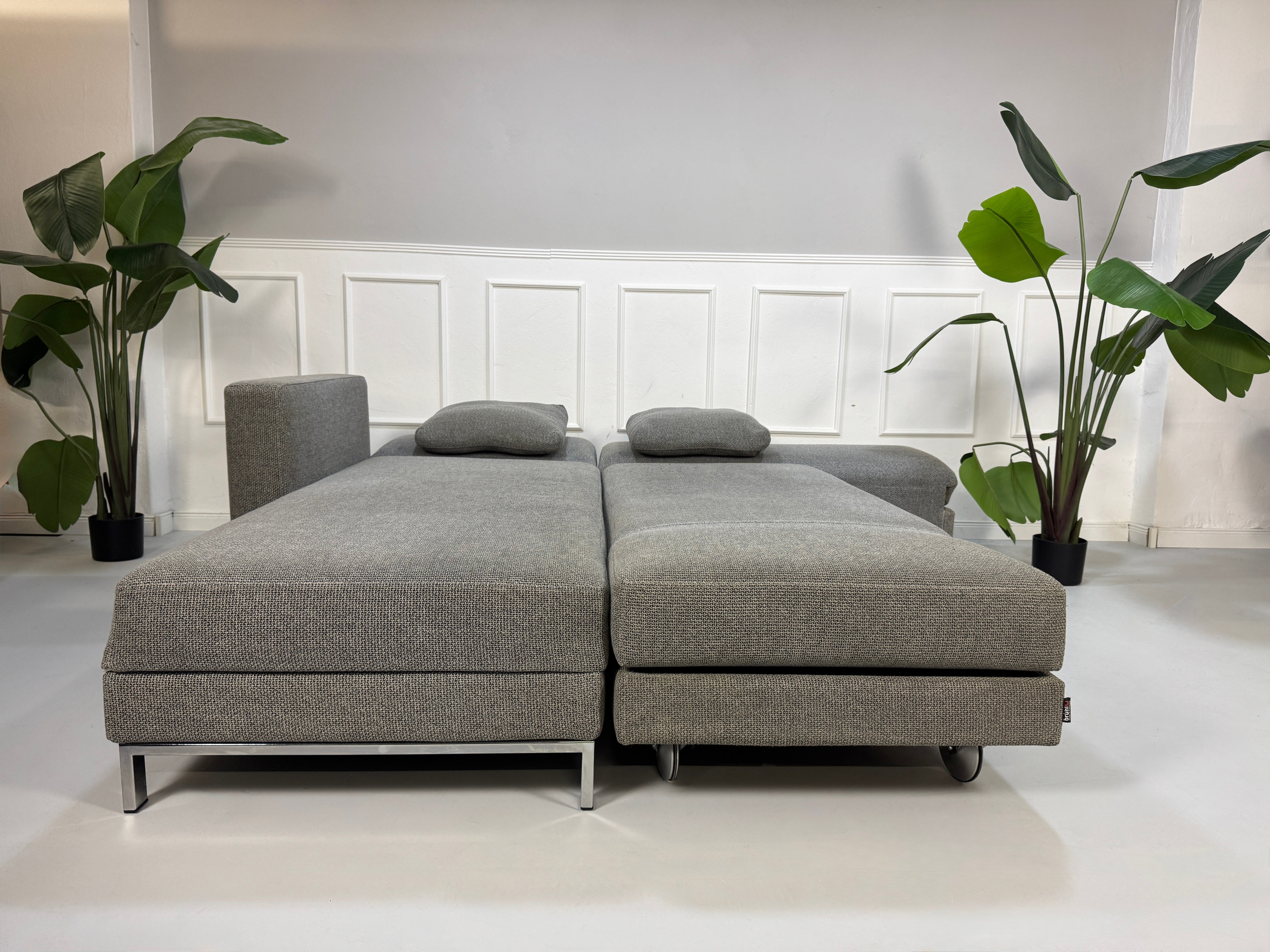 Gebrauchtes graues Brühl Fourtwo Designer Stoff Sofa vor einer Wand, stilvoll und modern eingerichtet.