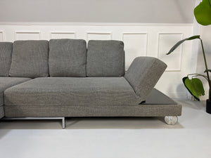 Gebrauchtes graues Brühl Fourtwo Designer Stoff Sofa vor einer Wand, stilvoll und modern eingerichtet.
