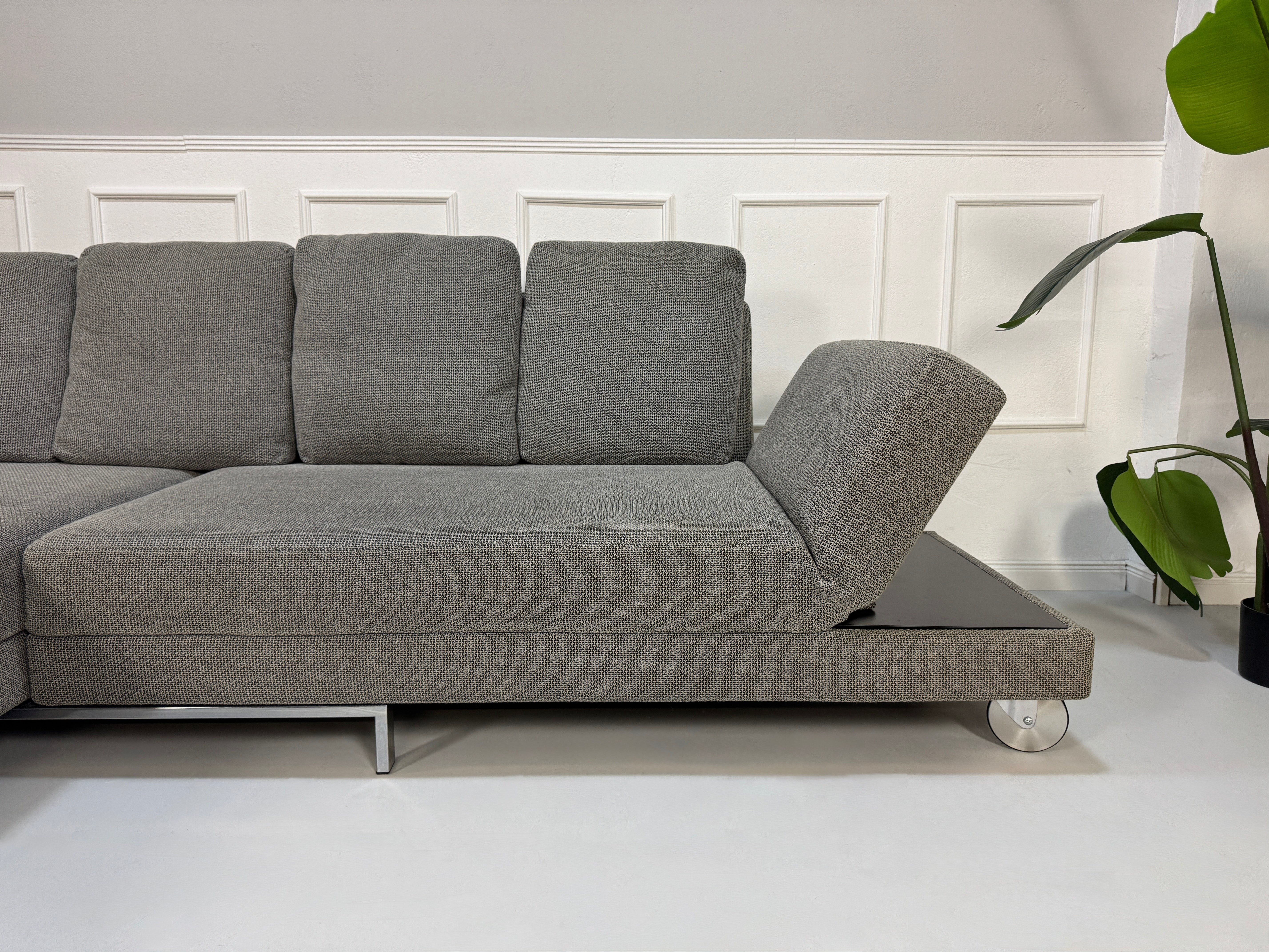 Gebrauchtes graues Brühl Fourtwo Designer Stoff Sofa vor einer Wand, stilvoll und modern eingerichtet.