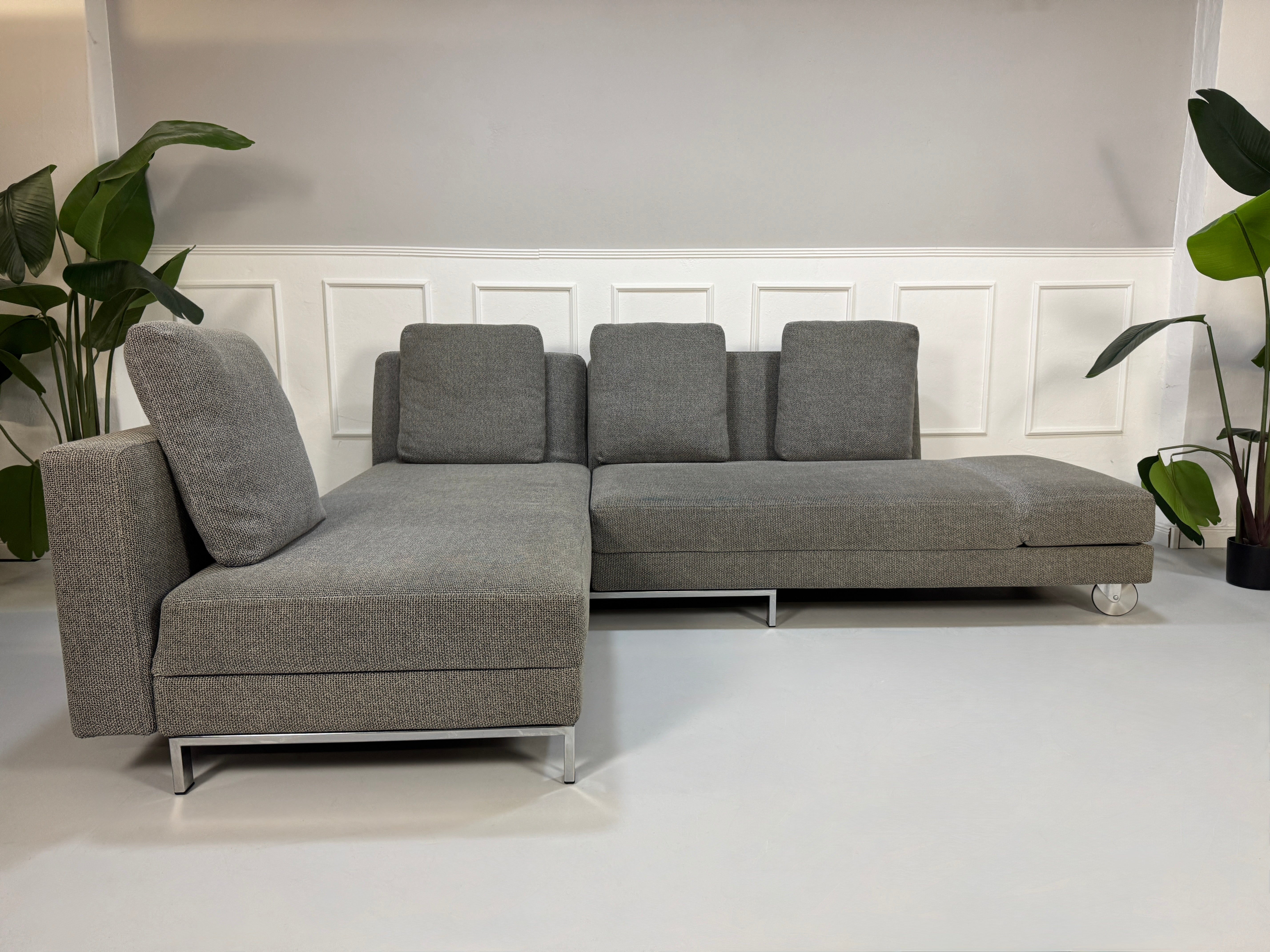 Gebrauchtes graues Brühl Fourtwo Designer Stoff Sofa vor einer Wand, stilvoll und modern eingerichtet.