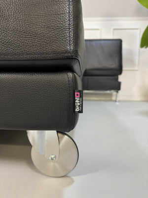 Gebrauchtes schwarzes Ledersofa Brühl Modell Four Two vor einer modernen Wand.