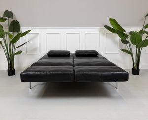 Gebrauchtes schwarzes Ledersofa Brühl Roro Soft vor einer modernen Wand.