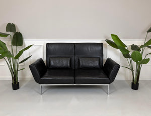 Gebrauchtes schwarzes Ledersofa Brühl Roro Soft vor einer modernen Wand.