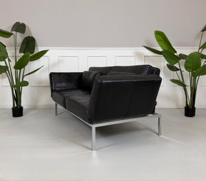 Gebrauchtes schwarzes Ledersofa Brühl Roro Soft vor einer modernen Wand.