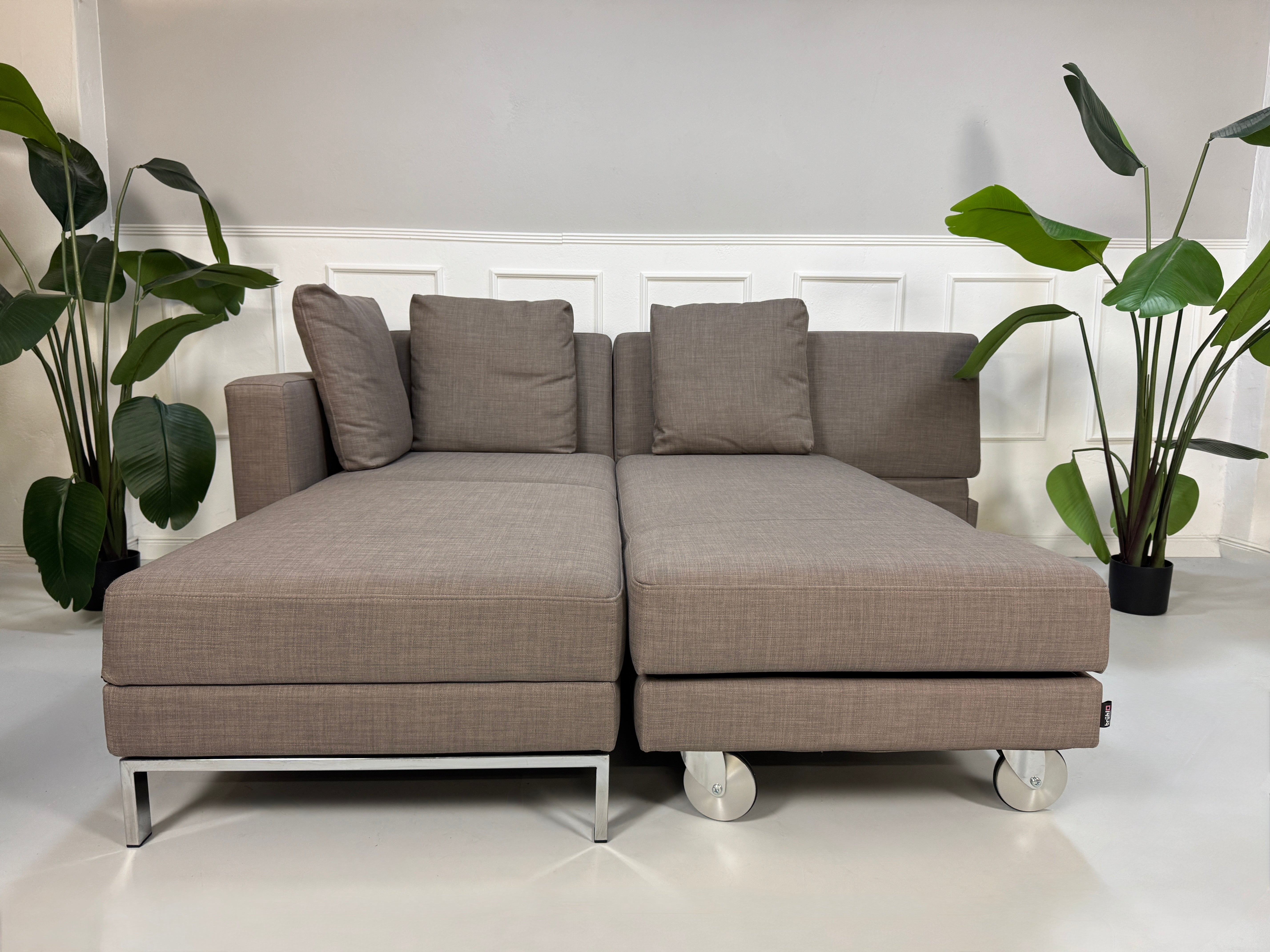 Gebrauchtes braunes Brühl Fourtwo Designer Stoff Sofa vor einer Wand, stilvoll und modern eingerichtet.