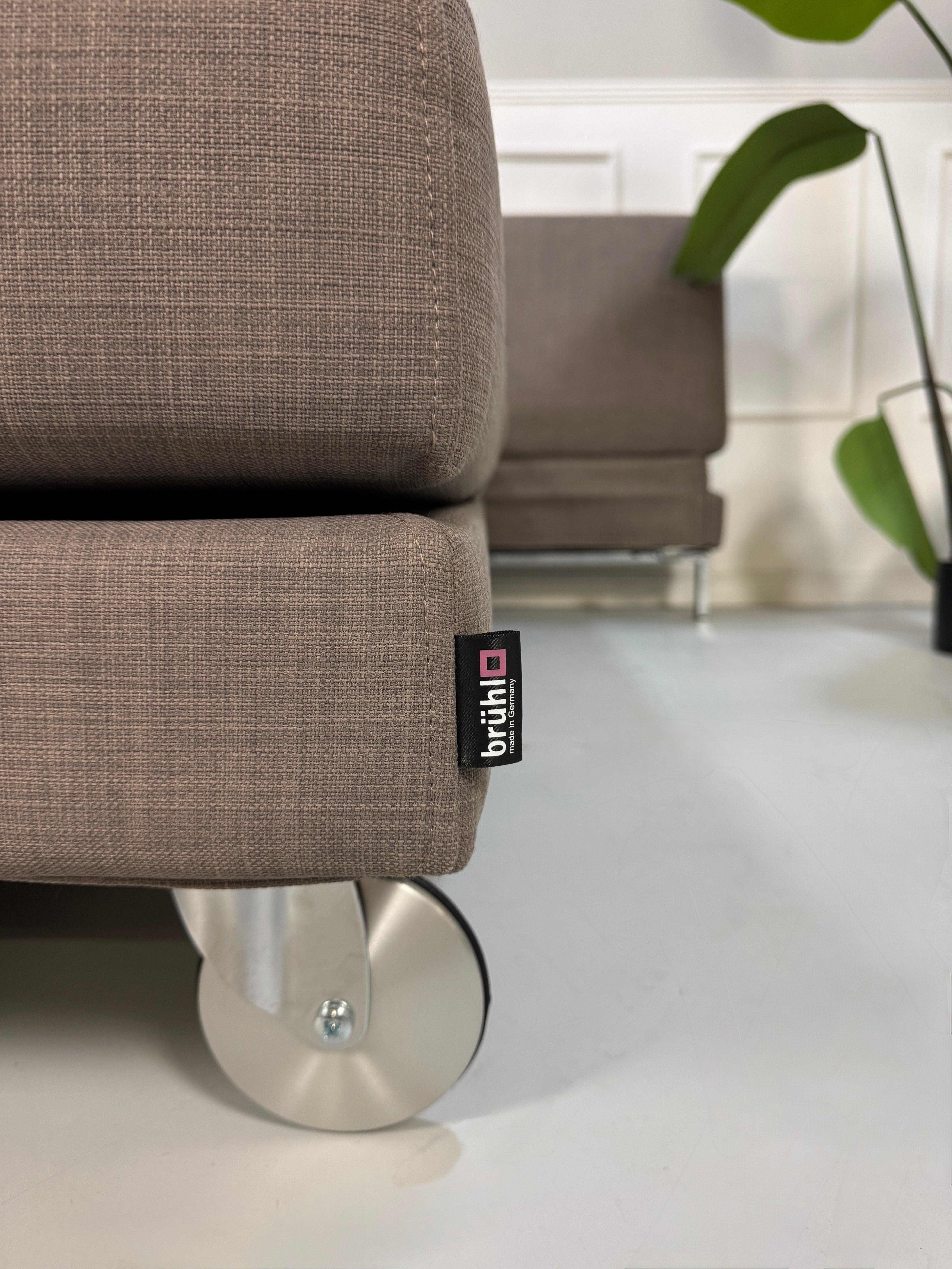 Gebrauchtes braunes Brühl Fourtwo Designer Stoff Sofa vor einer Wand, stilvoll und modern eingerichtet.