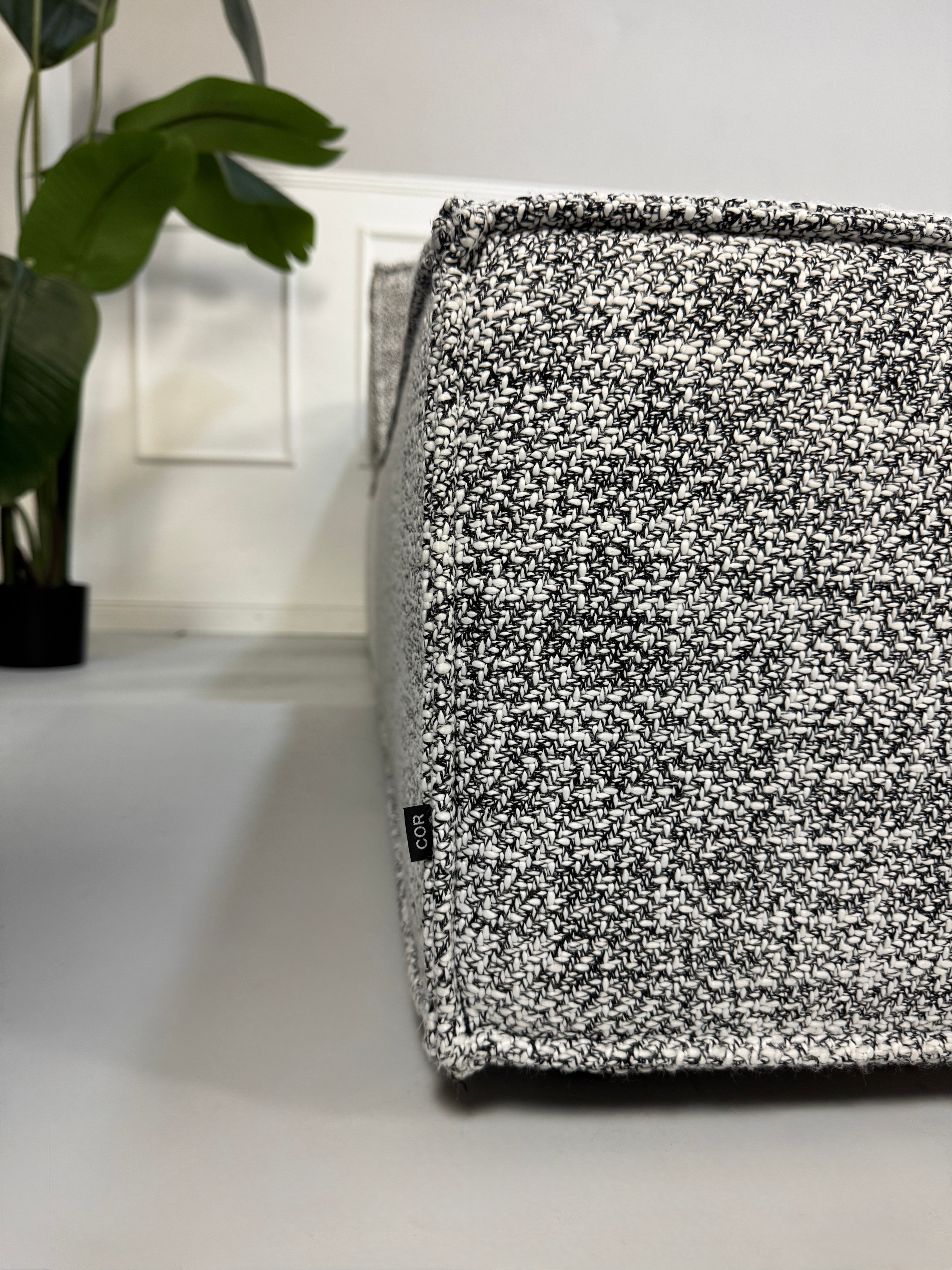 Gebrauchtes graues COR Trio Designer Stoff Sofa vor einer Wand, stilvoll und modern eingerichtet.