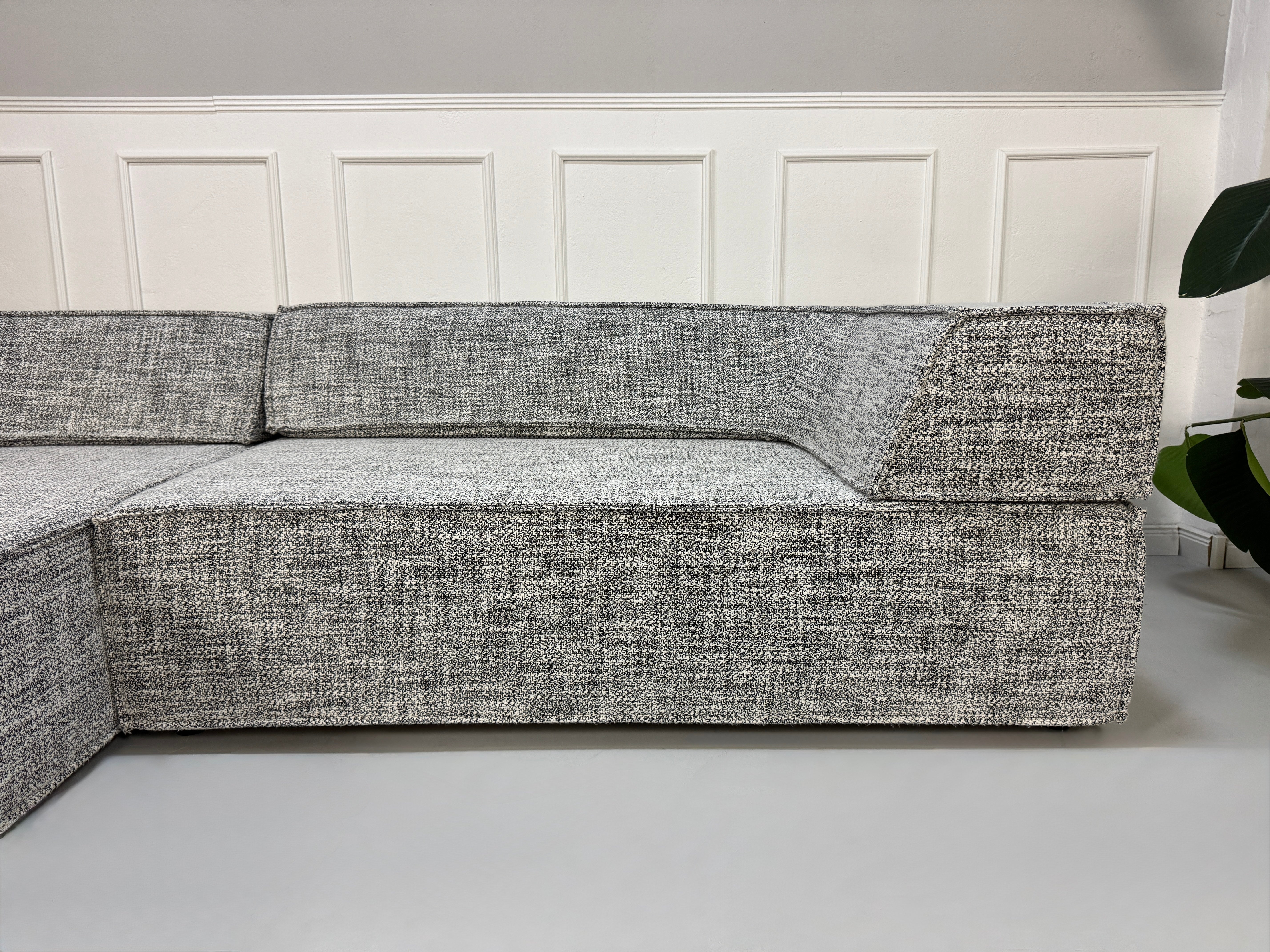 Gebrauchtes graues COR Trio Designer Stoff Sofa vor einer Wand, stilvoll und modern eingerichtet.