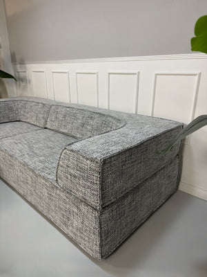Gebrauchtes graues COR Trio Designer Stoff Sofa vor einer Wand, stilvoll und modern eingerichtet.