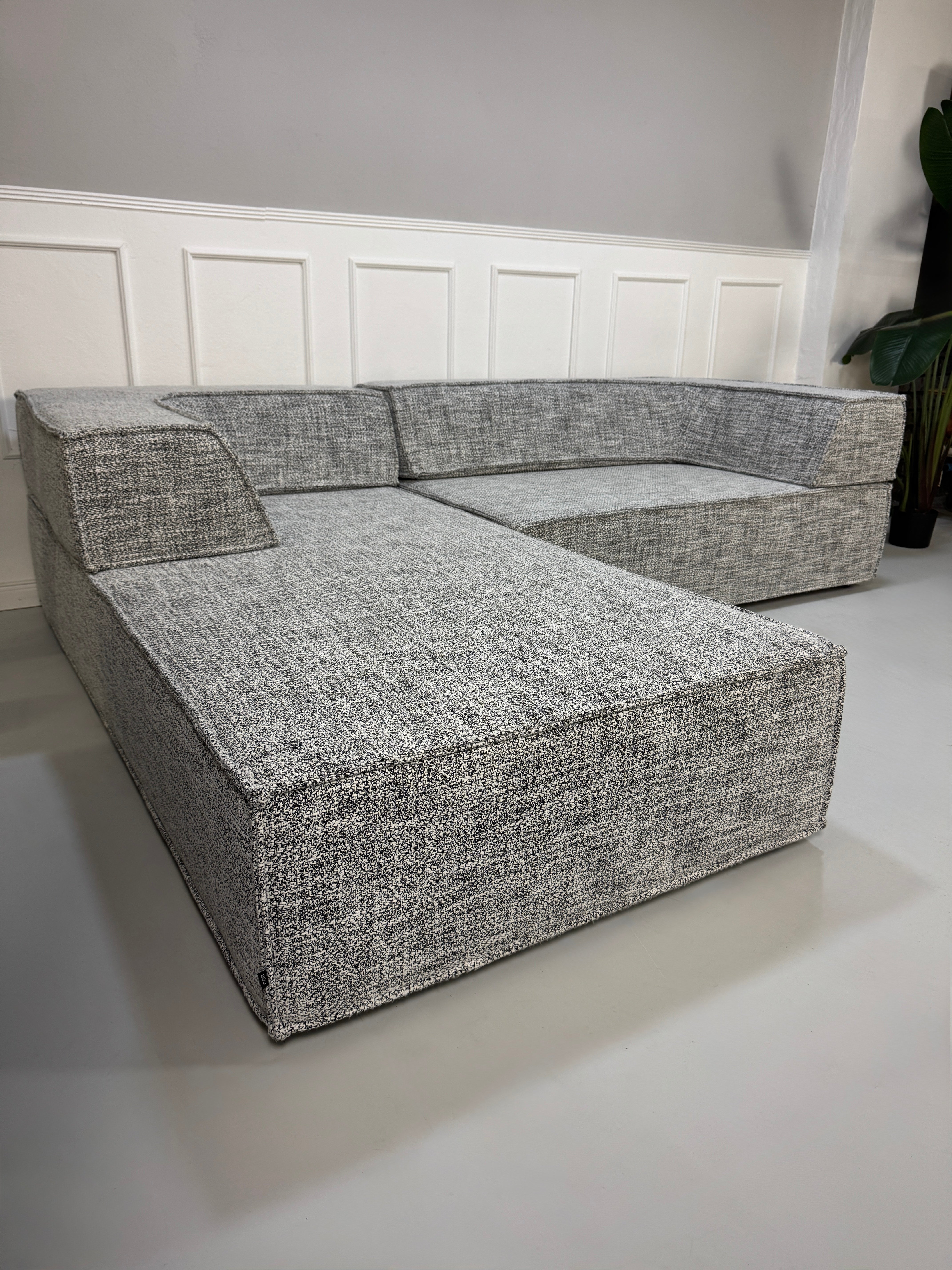 Gebrauchtes graues COR Trio Designer Stoff Sofa vor einer Wand, stilvoll und modern eingerichtet.