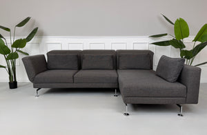 Gebrauchtes graues Stoffsofa Brühl Modell Moule vor einer modernen Wand.