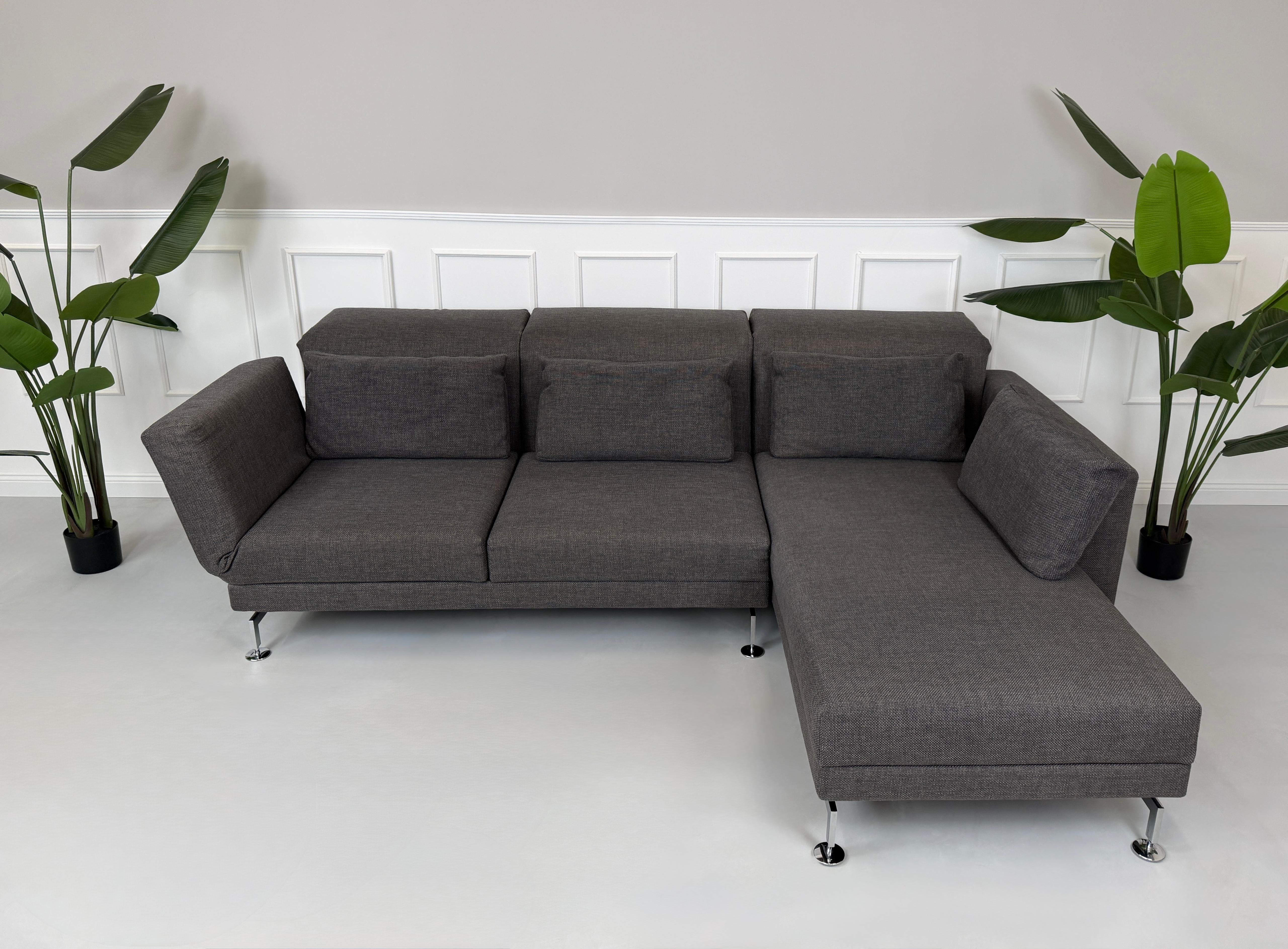 Gebrauchtes graues Stoffsofa Brühl Modell Moule vor einer modernen Wand.