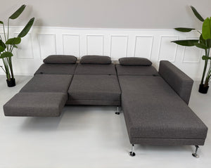 Gebrauchtes graues Stoffsofa Brühl Modell Moule vor einer modernen Wand.