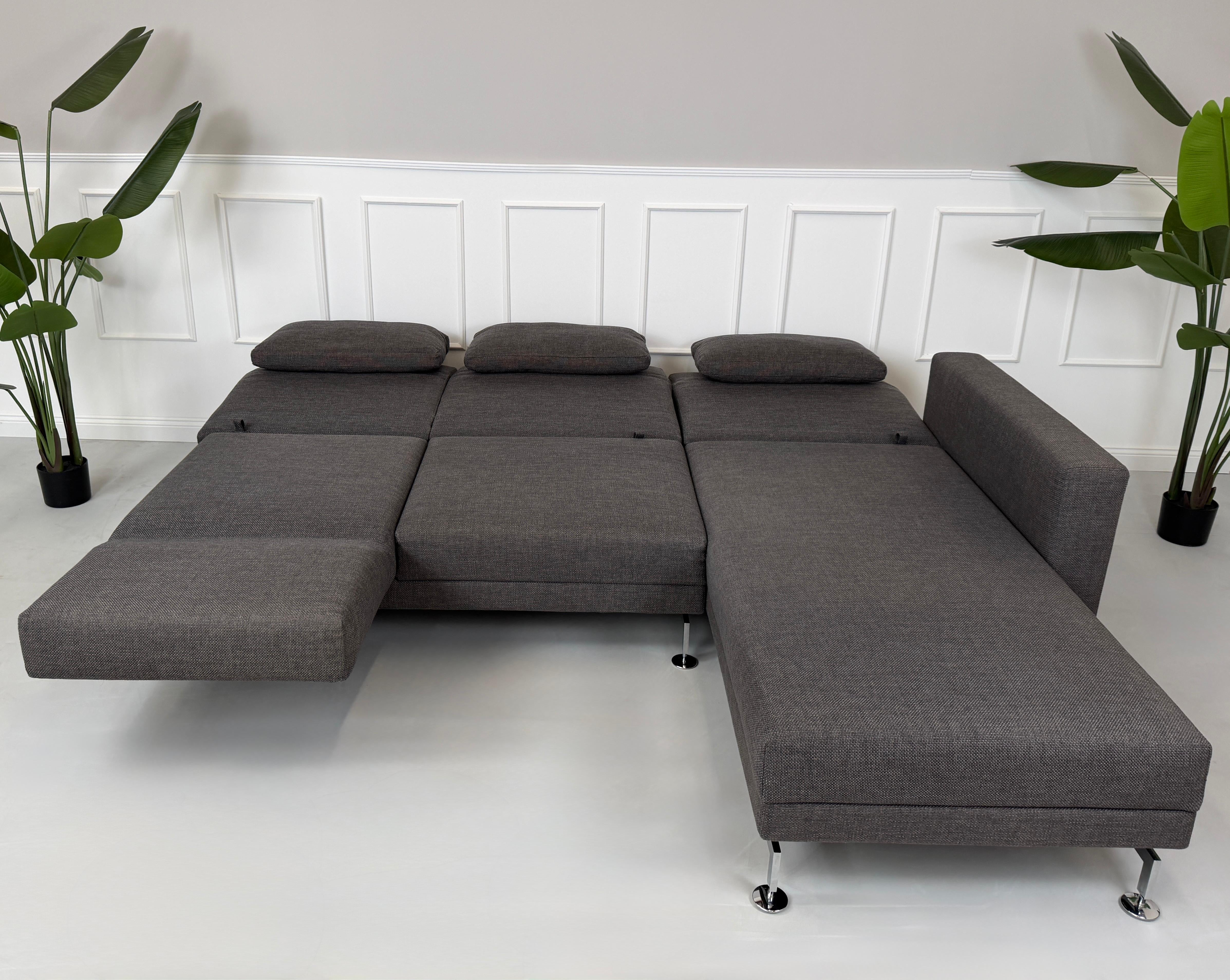 Gebrauchtes graues Stoffsofa Brühl Modell Moule vor einer modernen Wand.