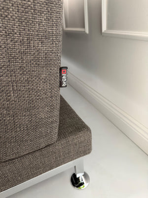 Gebrauchtes graues Stoffsofa Brühl Modell Moule vor einer modernen Wand.