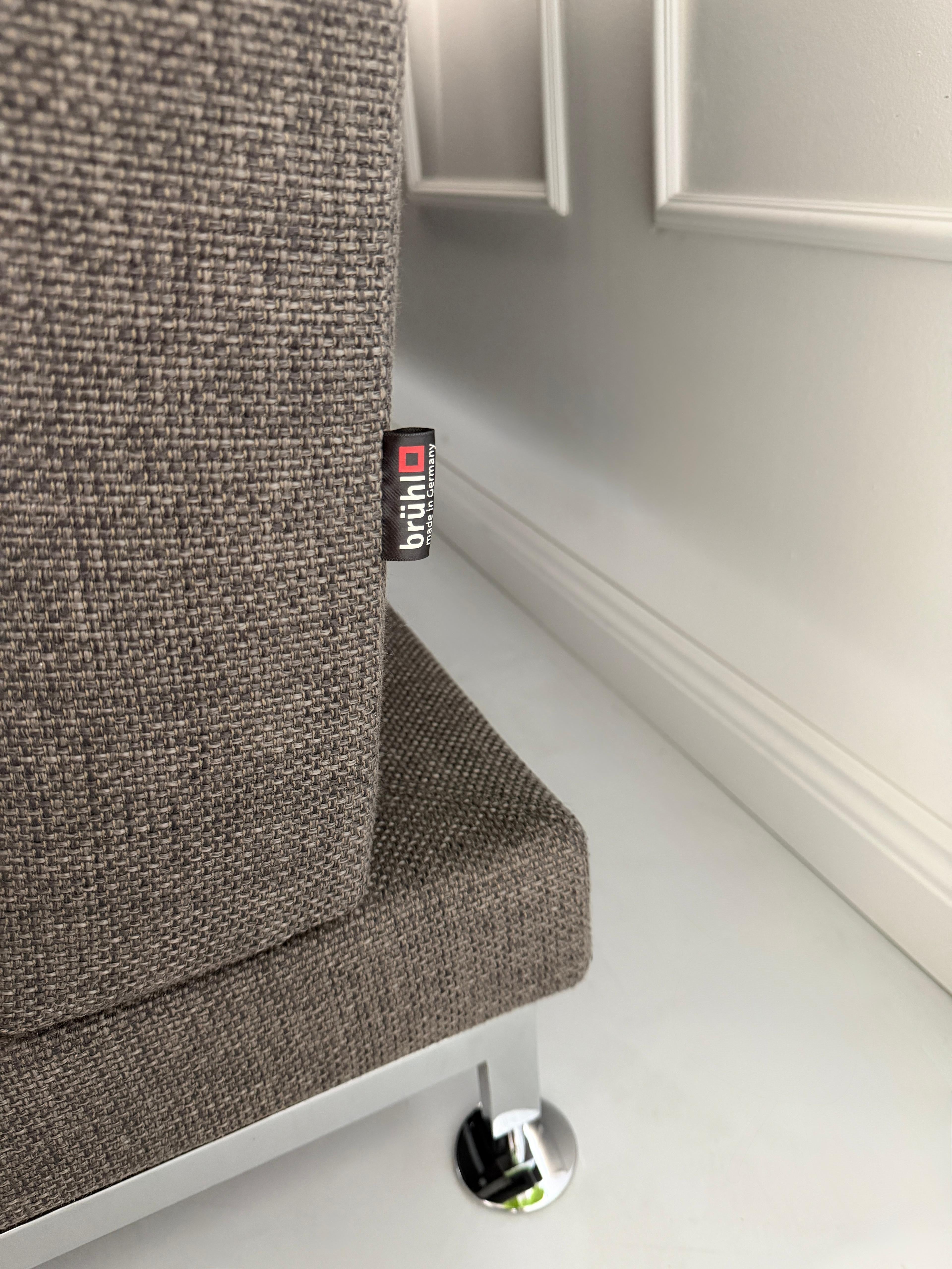 Gebrauchtes graues Stoffsofa Brühl Modell Moule vor einer modernen Wand.