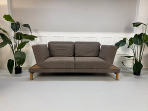 Gebrauchtes braunes Brühl Moule Designer Stoff Sofa vor einer Wand, stilvoll und modern eingerichtet.