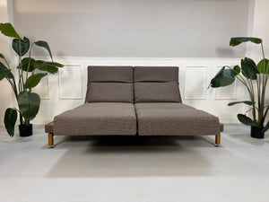 Gebrauchtes braunes Brühl Moule Designer Stoff Sofa vor einer Wand, stilvoll und modern eingerichtet.