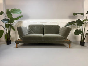 Gebrauchtes grün-graues Stoff Sofa Brühl Modell Moule Large vor einer modernen Wand.
