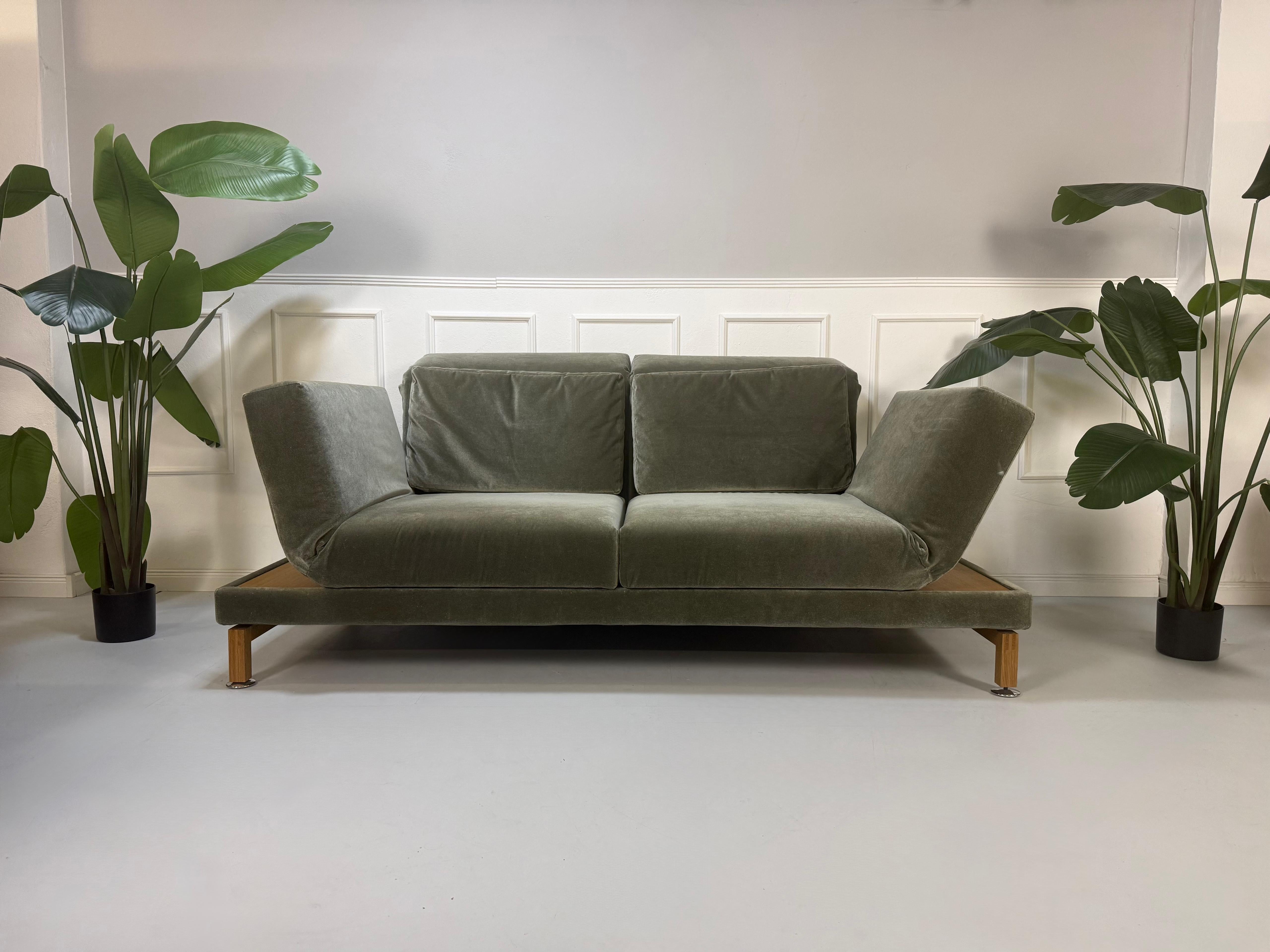 Gebrauchtes grün-graues Stoff Sofa Brühl Modell Moule Large vor einer modernen Wand.
